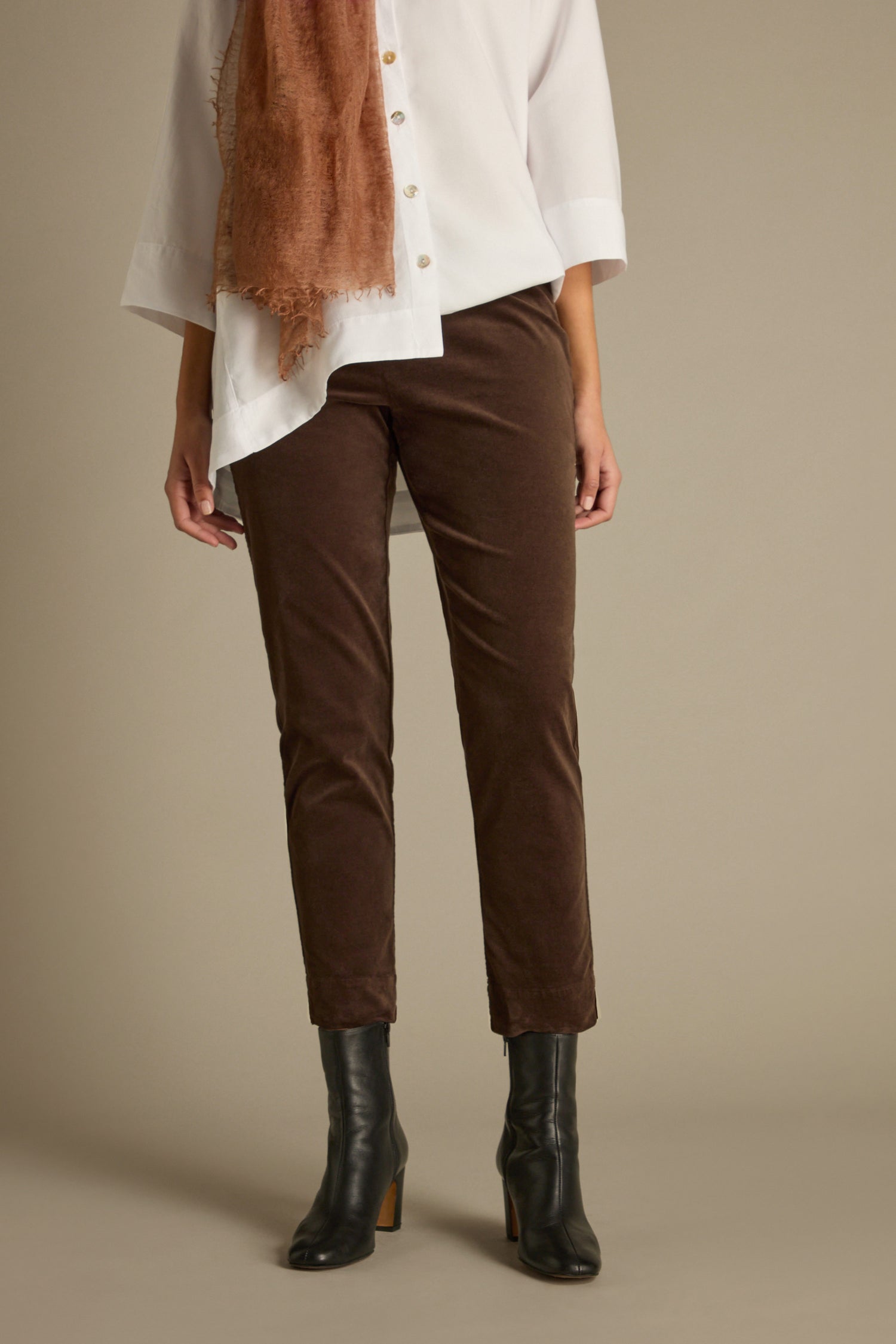 A person wearing a white shirt, brown scarf, and black boots stands against a neutral background, elegantly clad in tailored fit Cotton Moleskin Slim Trouser.