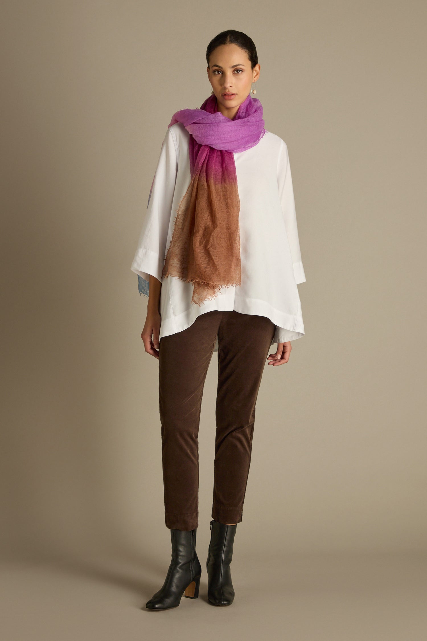 Against a plain background, someone stands dressed in a white blouse, Cotton Moleskin Slim Trousers in a tailored fit brown shade, black boots, and a multicolored scarf. These trousers are a wardrobe staple, effortlessly combining comfort and style.