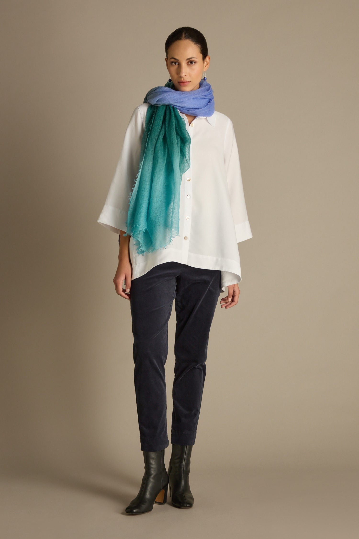 A person wearing a white top and the Cotton Moleskin Slim Trouser featuring an elasticated waistband, complemented by black boots and a turquoise-blue scarf, stands against a plain background.