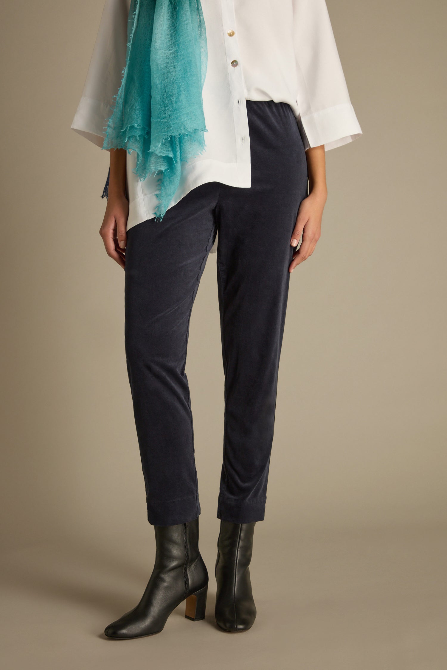 A person wearing a white shirt, a teal scarf, and the Cotton Moleskin Slim Trouser in a tailored fit stands against a plain background, completing the look with black heeled boots.
