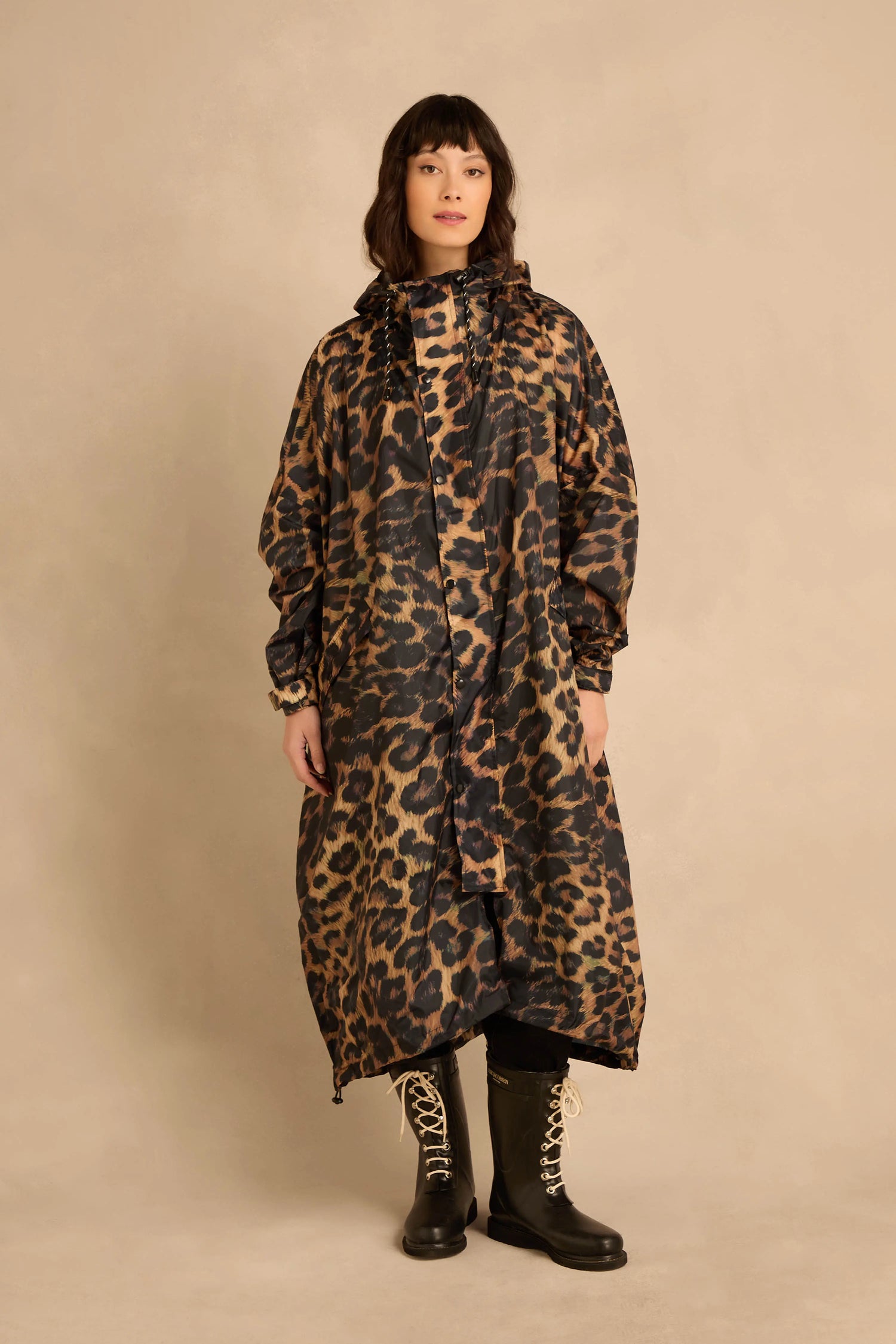 A person wearing an oversized Dark Leopard Rain Coat with a hood and black lace-up boots.