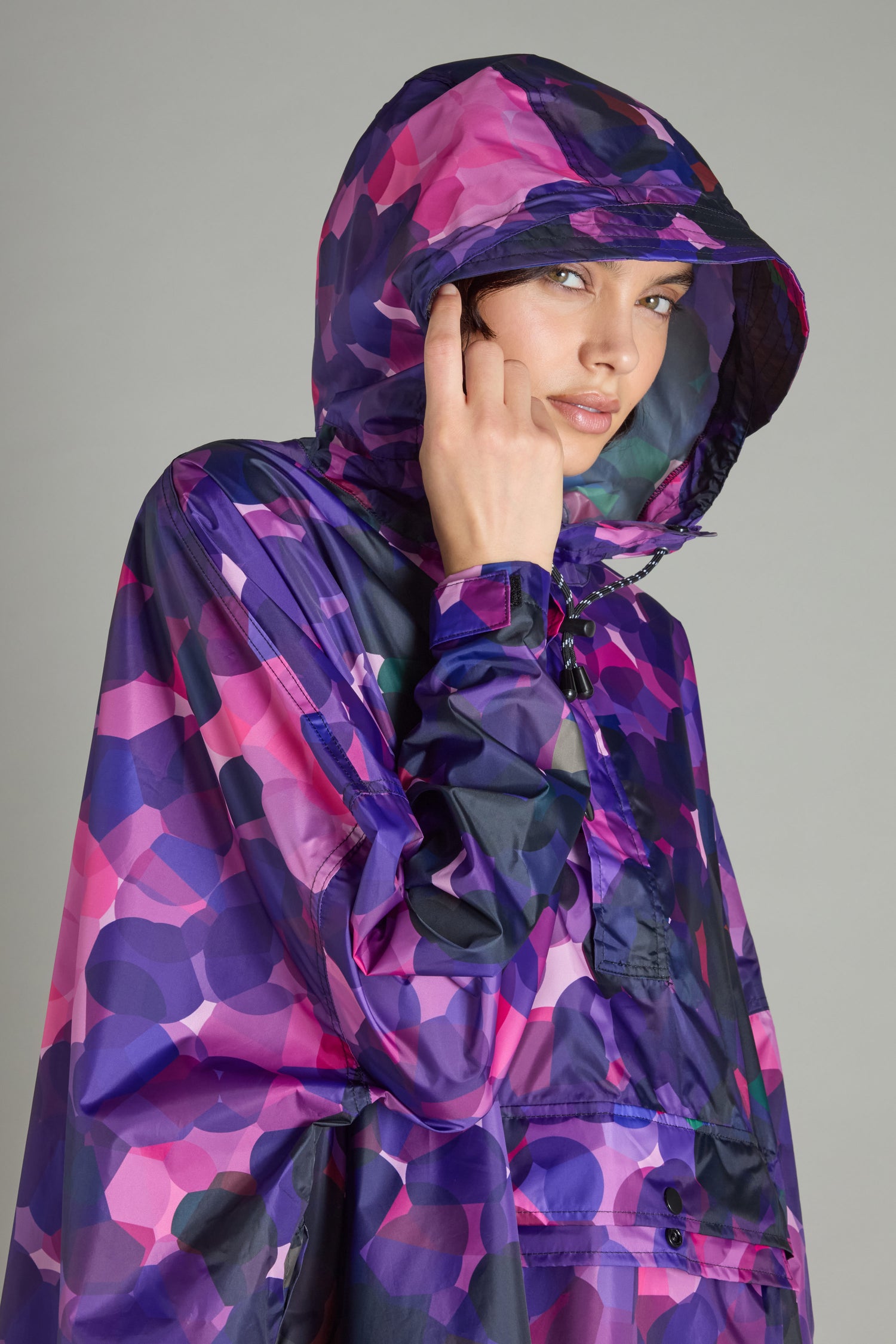Person wearing the City Lights Poncho, featuring a pink and purple geometric pattern with a hood, crafted from recycled plastic to showcase innovative urban design.