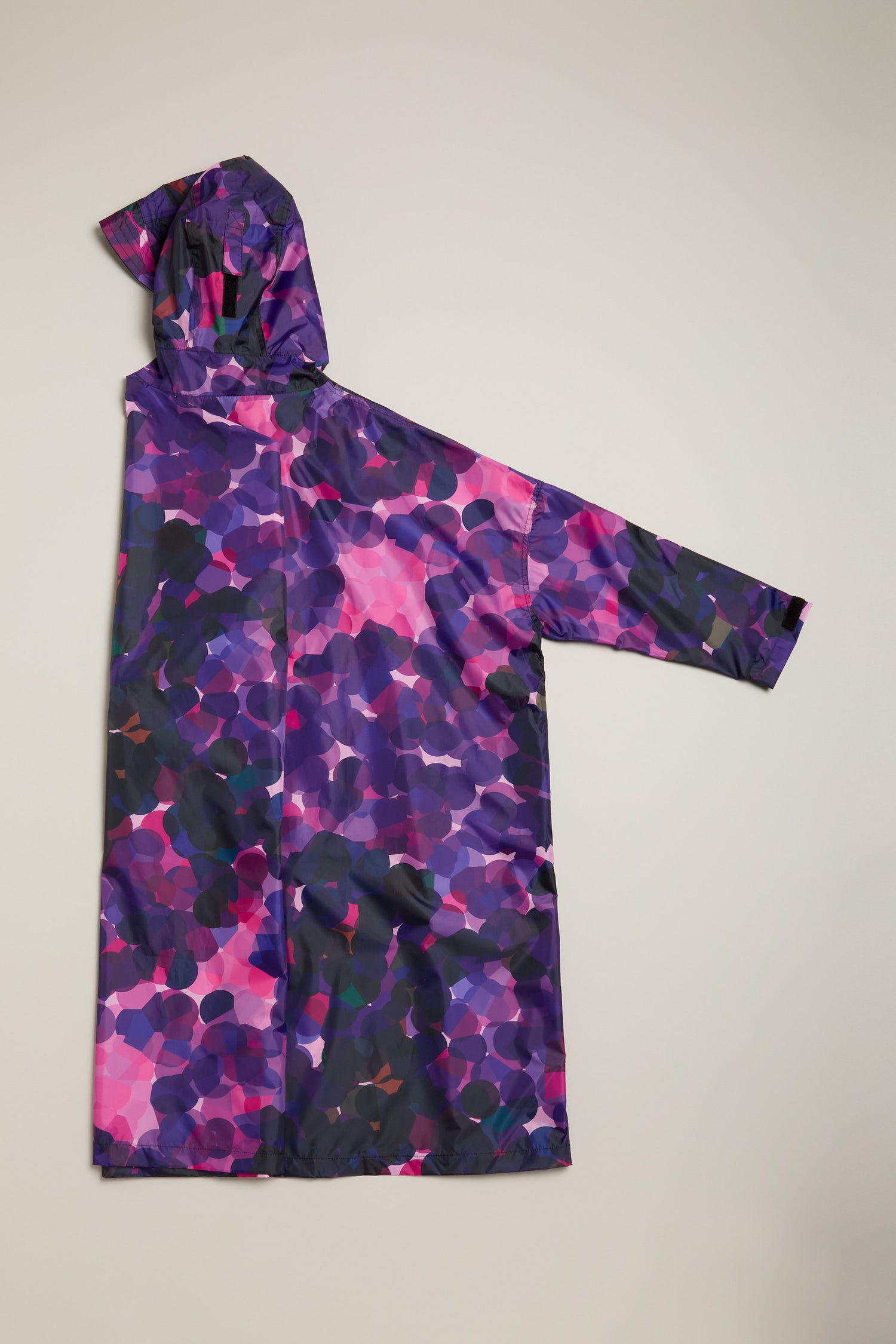 City Lights Poncho with a hood, made from recycled plastic, showcasing a vibrant pattern of purple, pink, and black abstract shapes against a plain background.