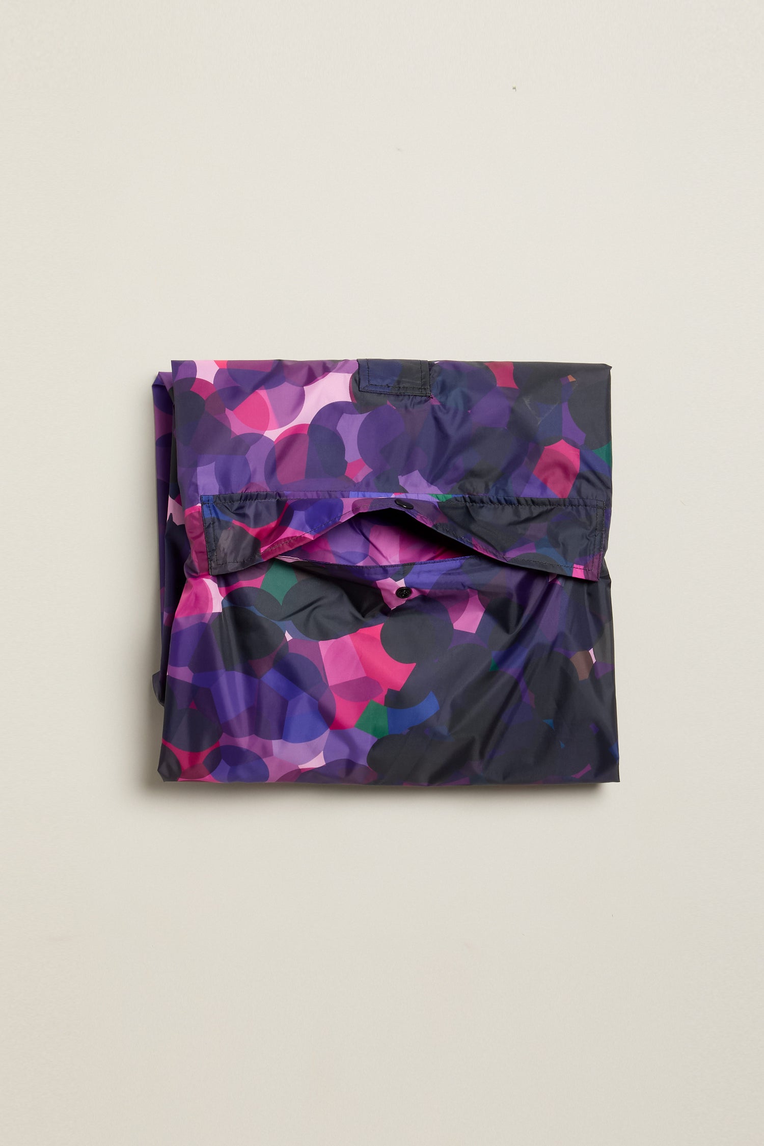 City Lights Poncho, crafted from recycled plastic, features a multicolored abstract pattern on a neutral background for an urban design edge.