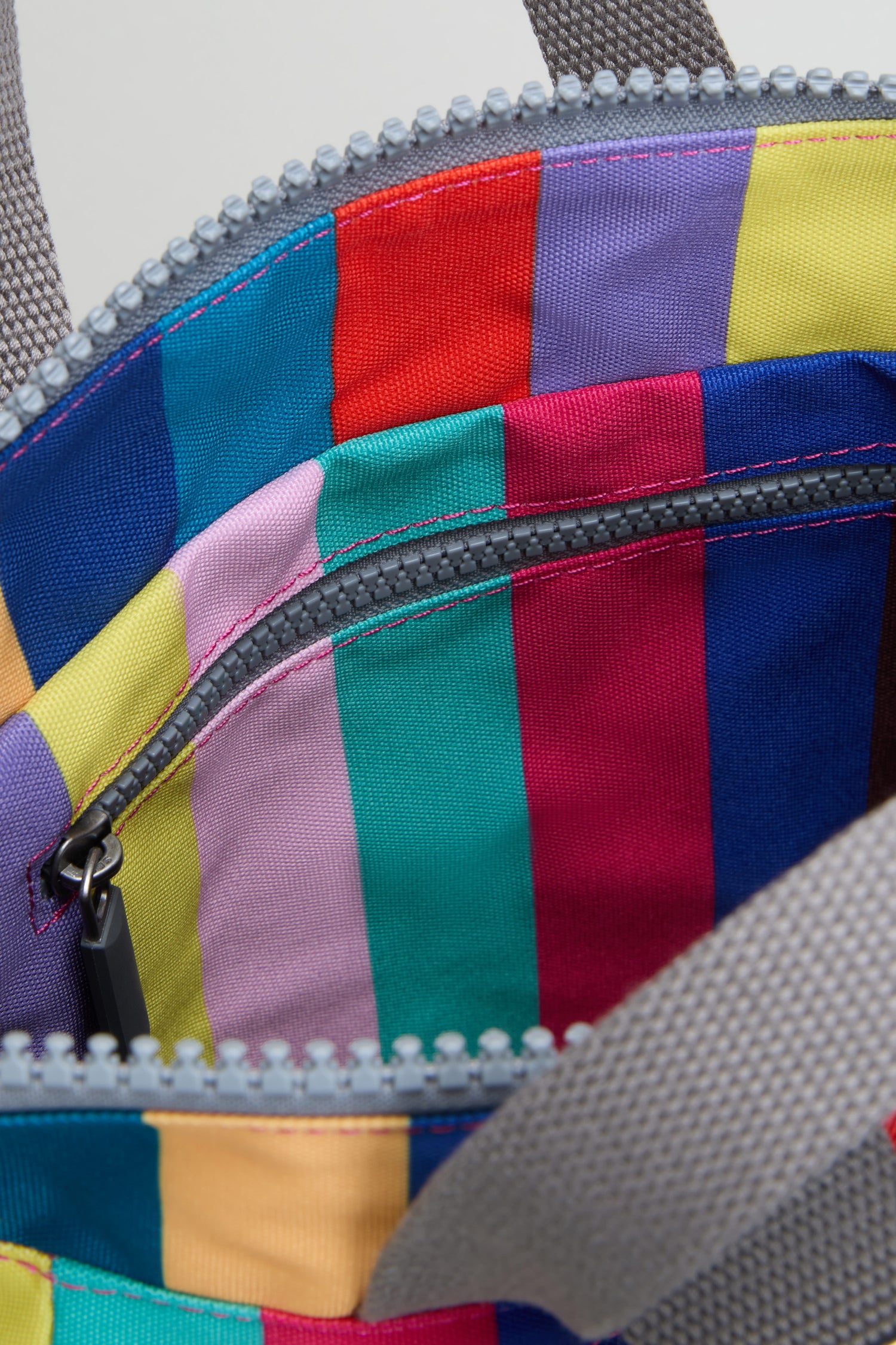 Close-up of the Wide Multistripe Bantry Canvas Bag featuring vibrant multicolored stripes, a noticeable gray zipper, and a portion of its gray woven strap.