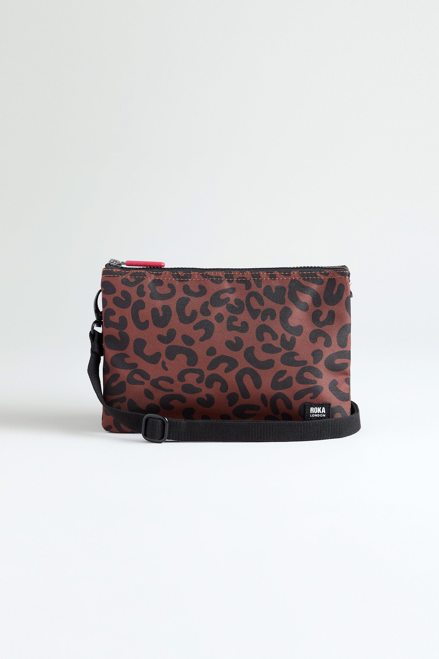 The Recycled Canvas Carnaby Leopard Crossbody Bag features a brown and black leopard print, black adjustable strap, small "RONA" logo near the bottom, and is crafted from recycled canvas in the signature ROKA style.