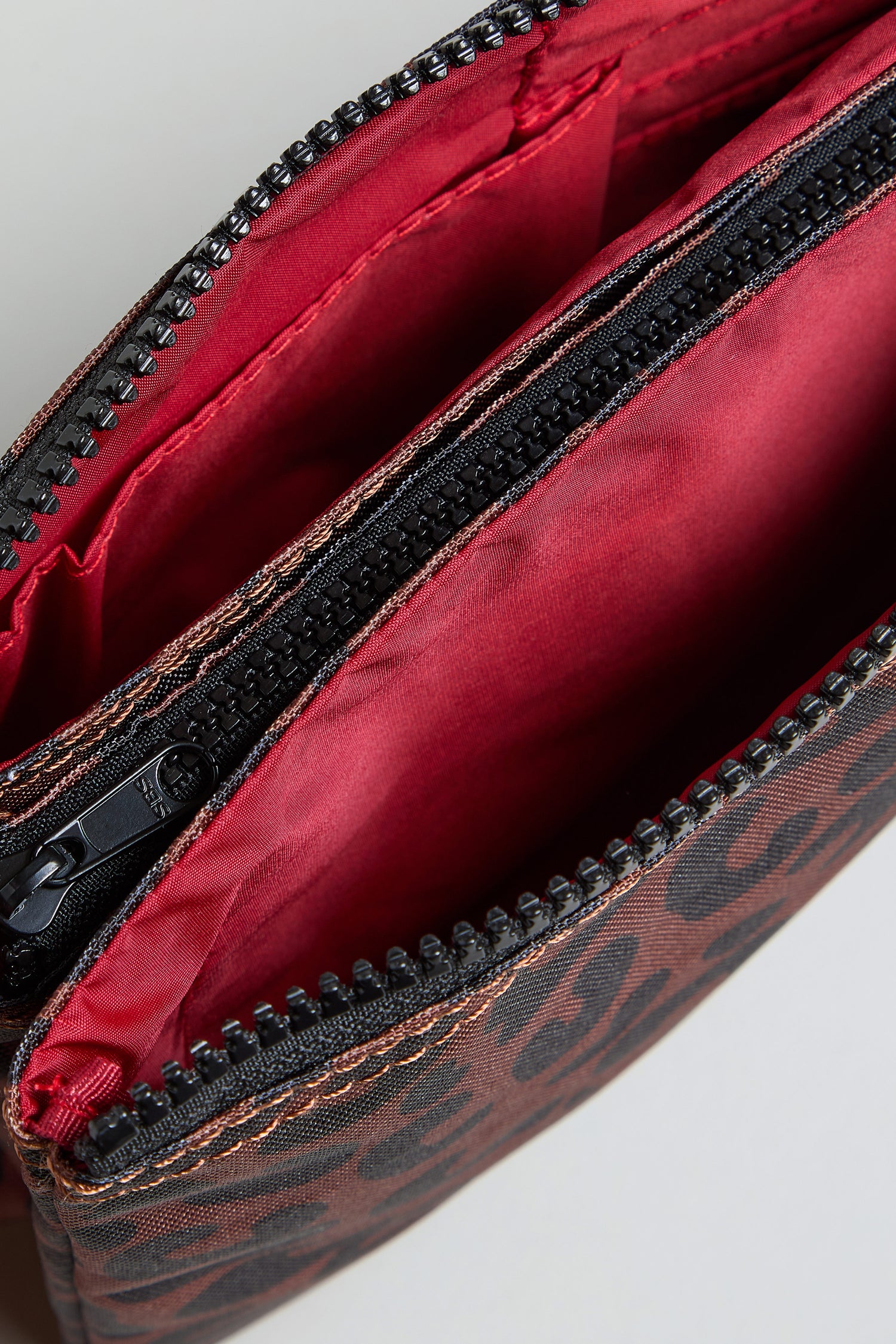 Close-up of the Recycled Canvas Carnaby Leopard Crossbody Bag with an open zippered pouch, featuring a red fabric interior and black and brown patterned exterior—stylish and eco-friendly.