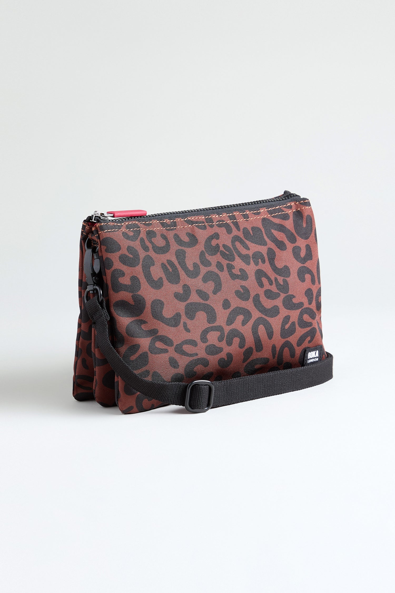 The Recycled Canvas Carnaby Leopard Crossbody Bag features a rectangular shape, red and black leopard print, black adjustable strap, and zipper closure, crafted from recycled canvas and shown against a plain white background.