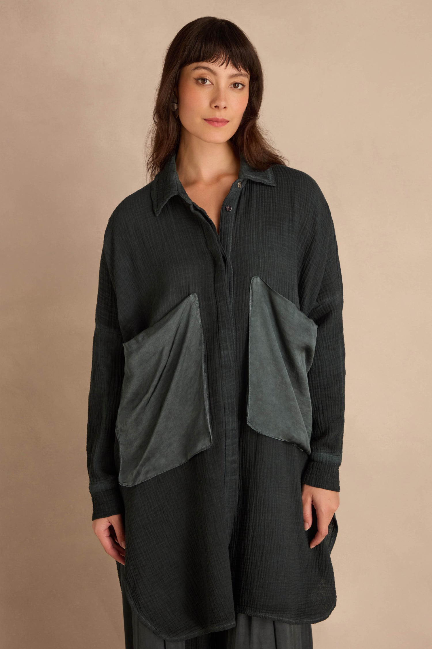 A model wears a dark green Petrol Pocket Satin Shirt featuring an oversized fit and two large, contrasting pockets on the front.