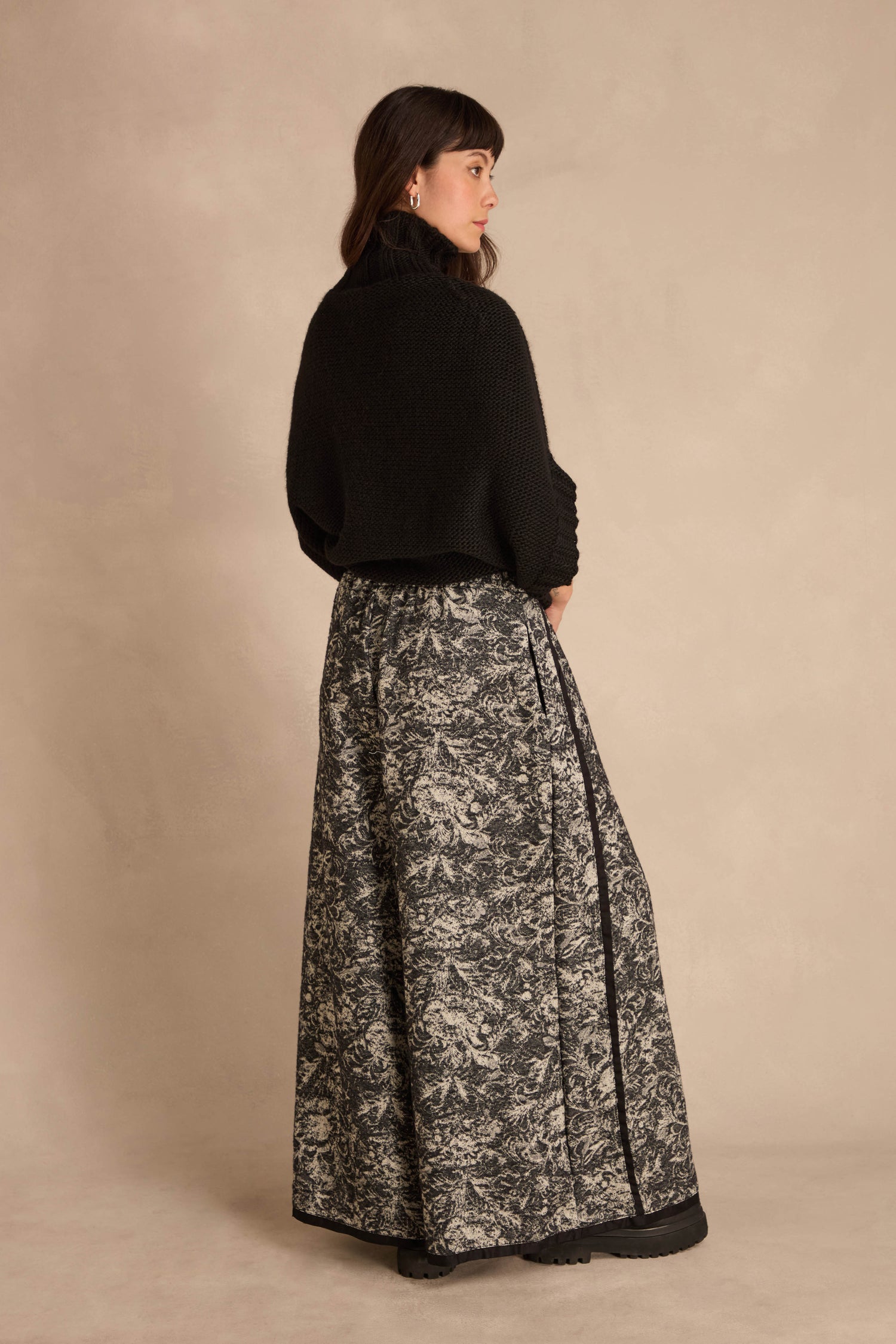 A person wearing a black mock-neck sweater and Frayed Hem Wide Leg Trousers in a floral pattern.