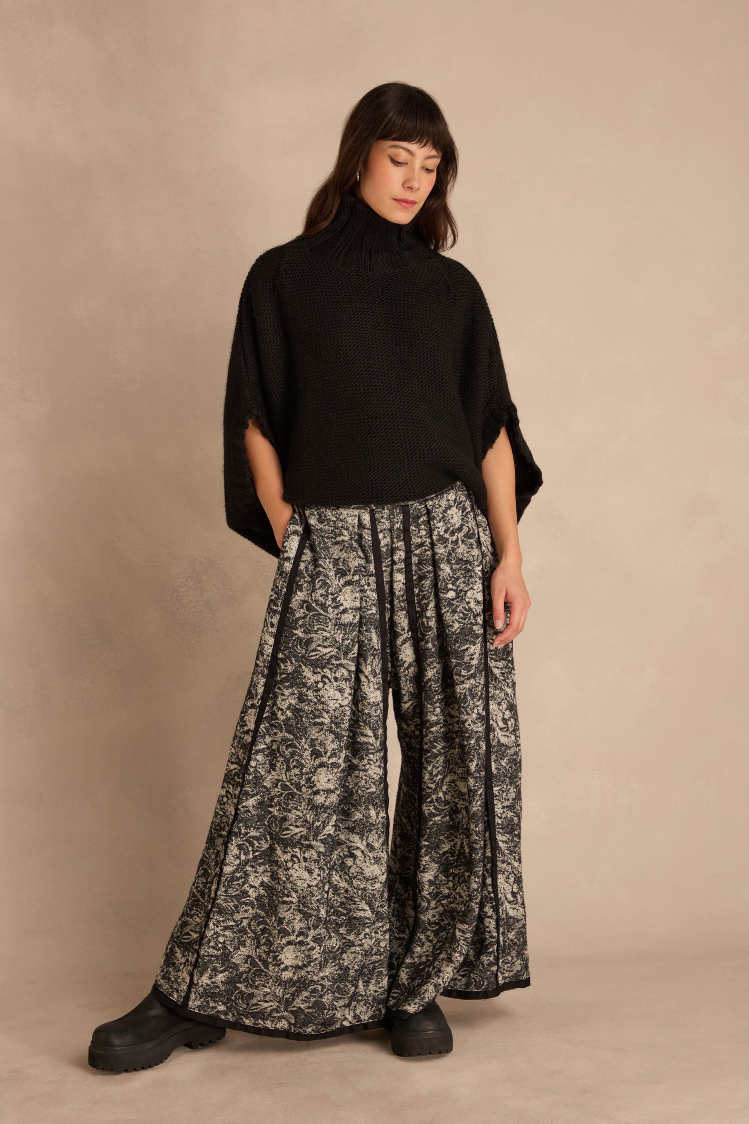 A person wears a black knitted poncho and Frayed Hem Wide Leg Trousers with a floral pattern and frayed hems.