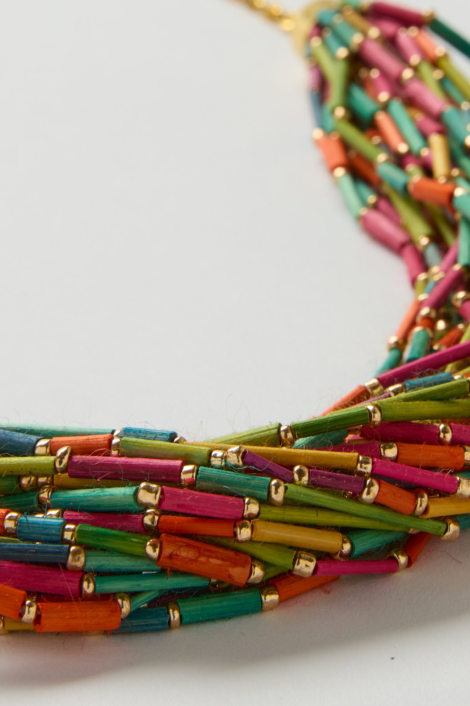 Close-up of the Multi Strand Grass Bead Necklace with vibrant green, pink, orange, red, and blue tubular beads, accented by small gold spacers and finished with a gold-look clasp chain.