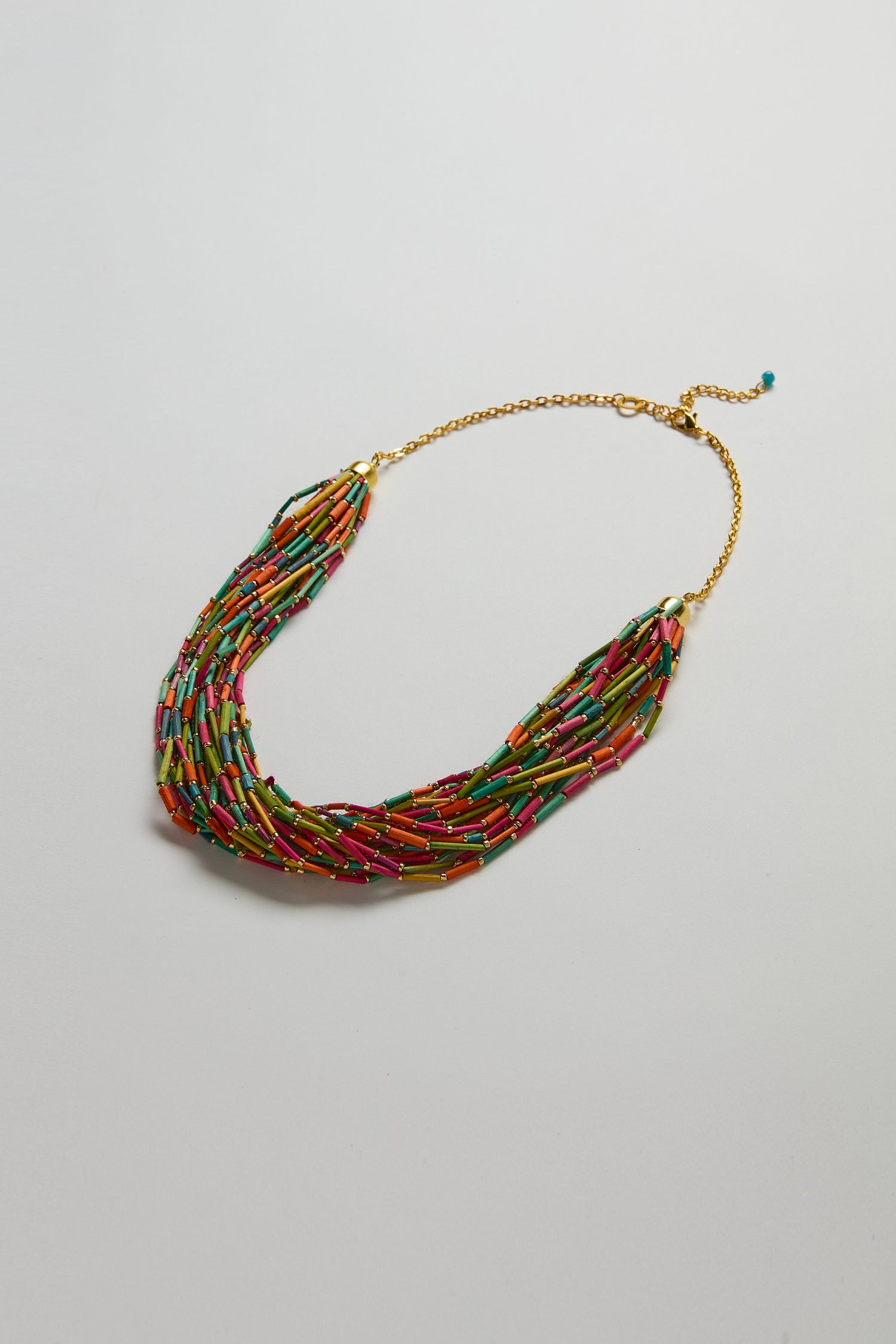 The Multi Strand Grass Bead Necklace has vibrant grass beads, a gold-look clasp chain, and an adjustable length, shown on a plain background.