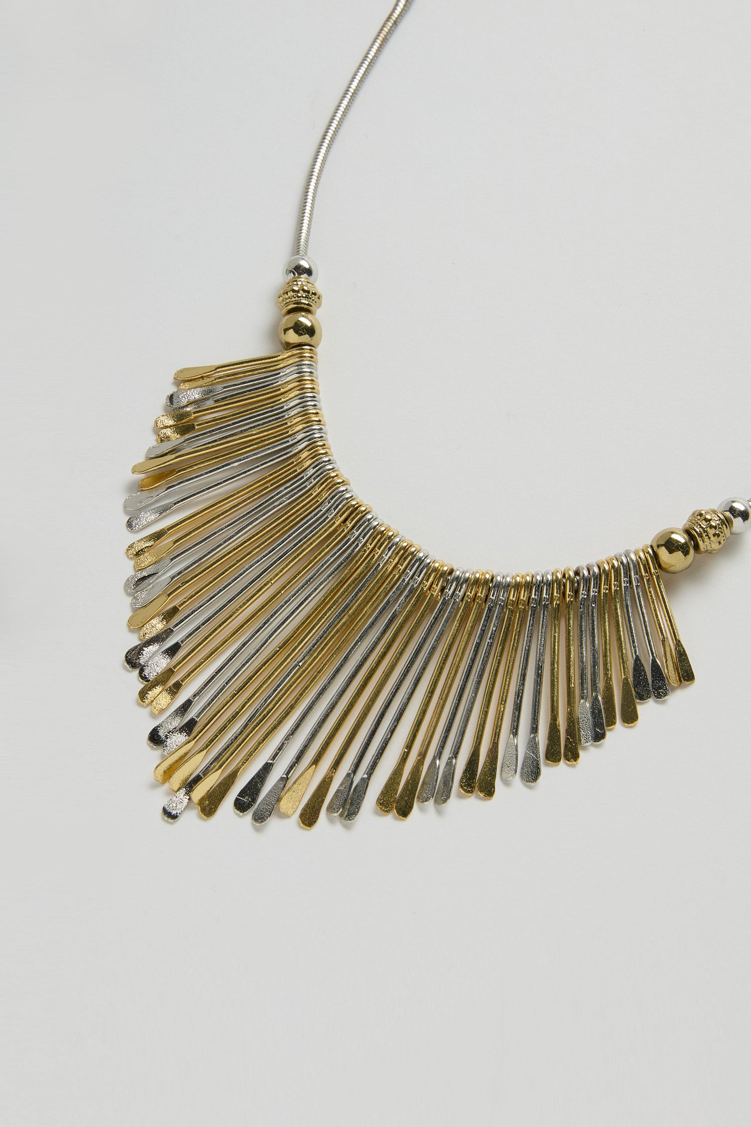 The Mixed Metal Fan Necklace showcases gold and silver-toned fringe pendants on a delicate silver chain, creating a bold contemporary look against a white background.