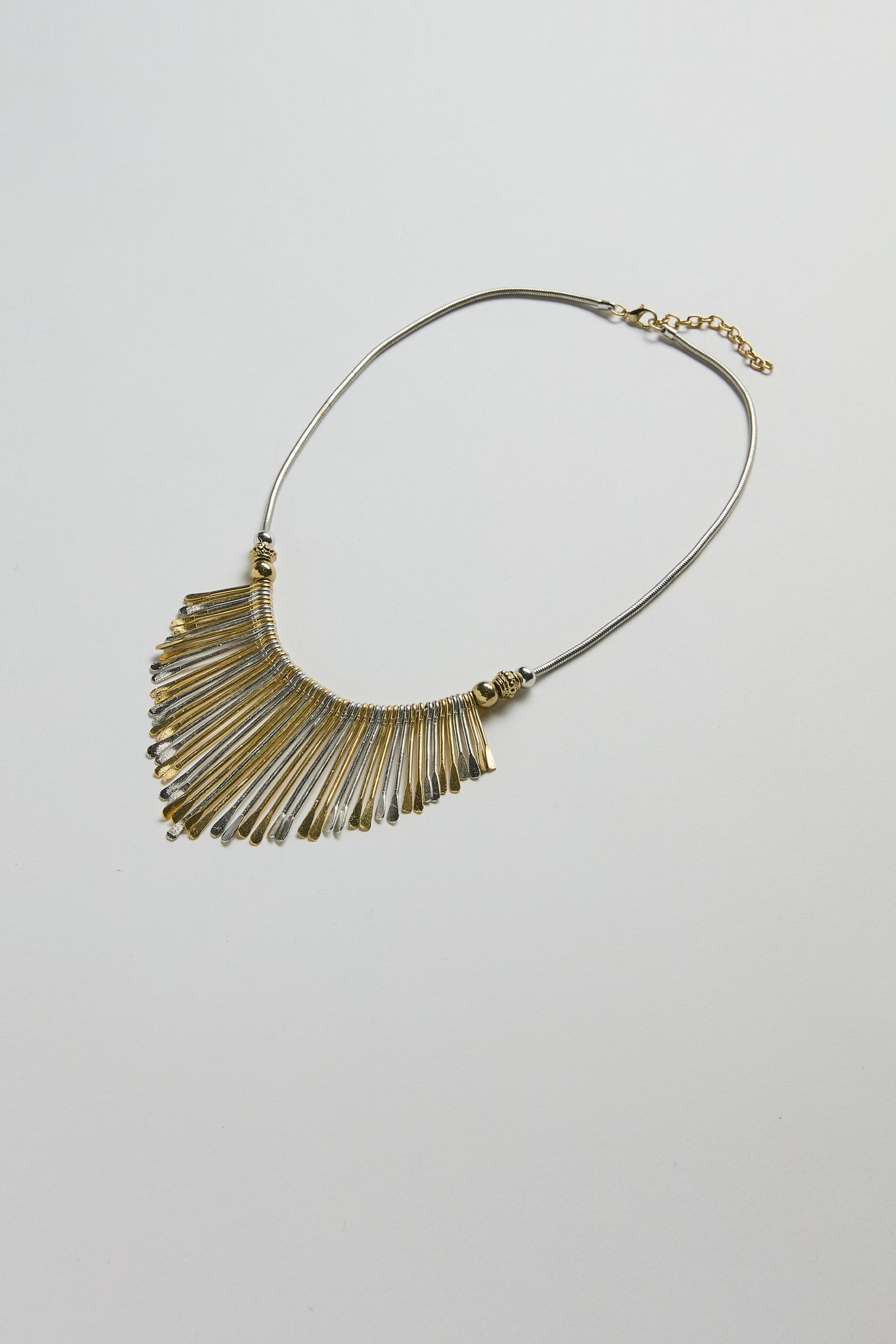 The Mixed Metal Fan Necklace features thin, elongated gold and silver-toned pendants in a fan shape, displayed on a plain white background.