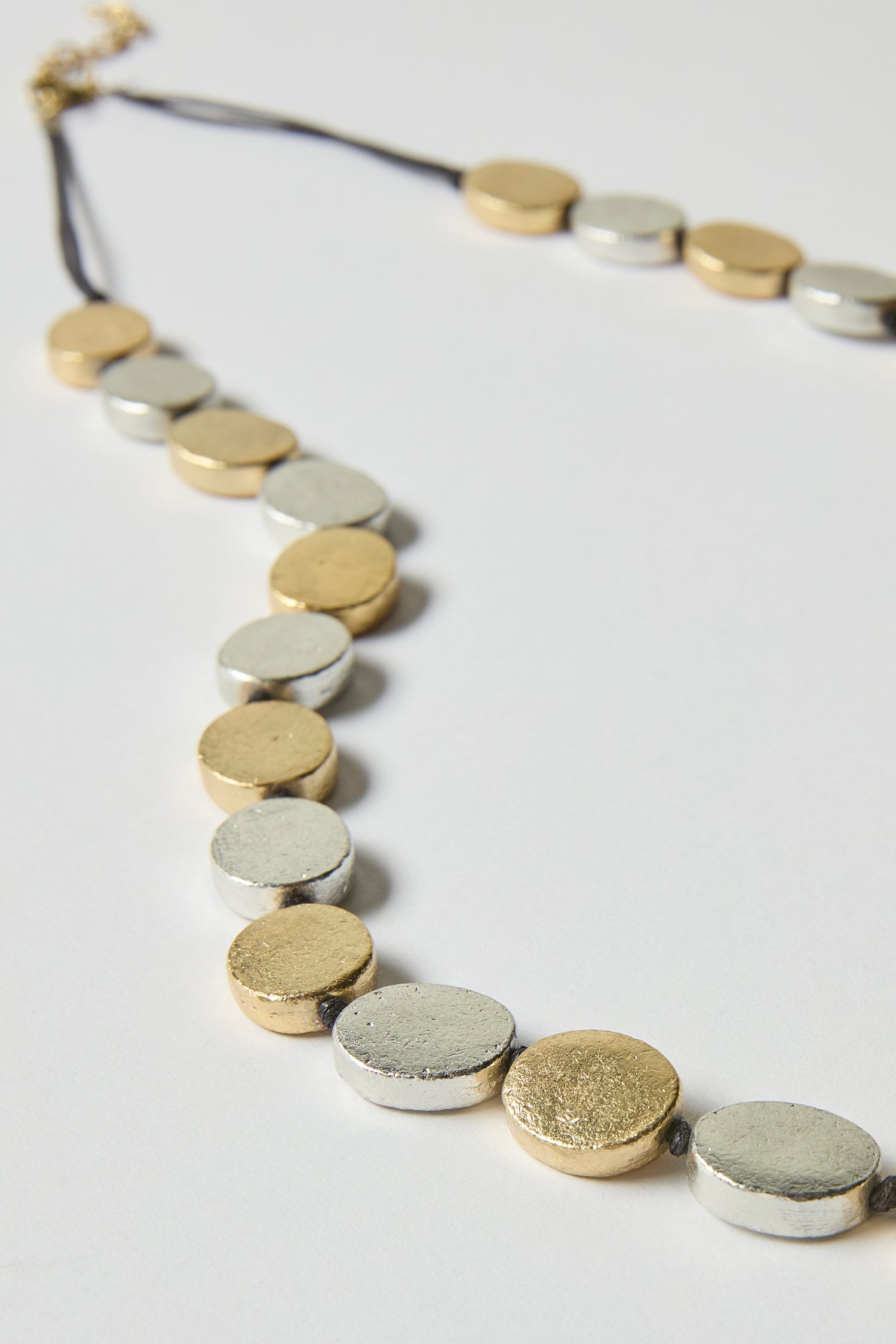 The Mixed Metal Disc Necklace showcases alternating silver and gold round beads on a black cord, elegantly set against a white background—an ideal addition to any timeless jewellery collection.