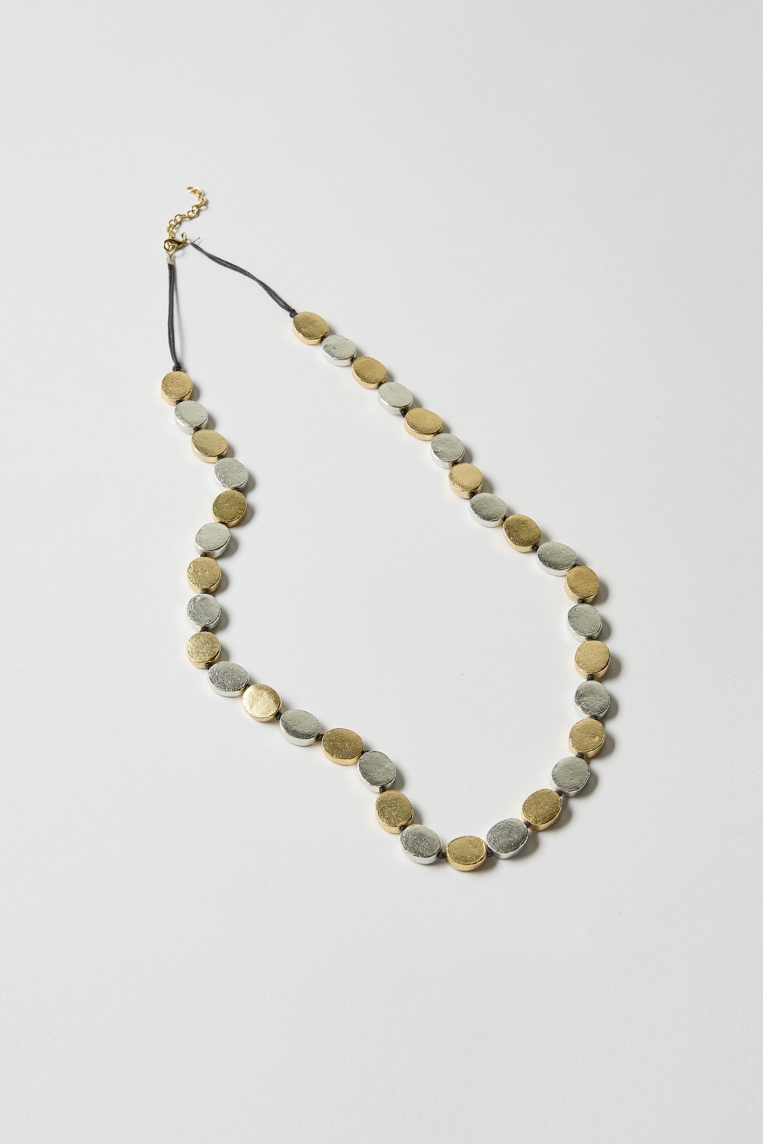 The Mixed Metal Disc Necklace showcases alternating silver and gold-finished round discs on a black cord, set against a plain white background.