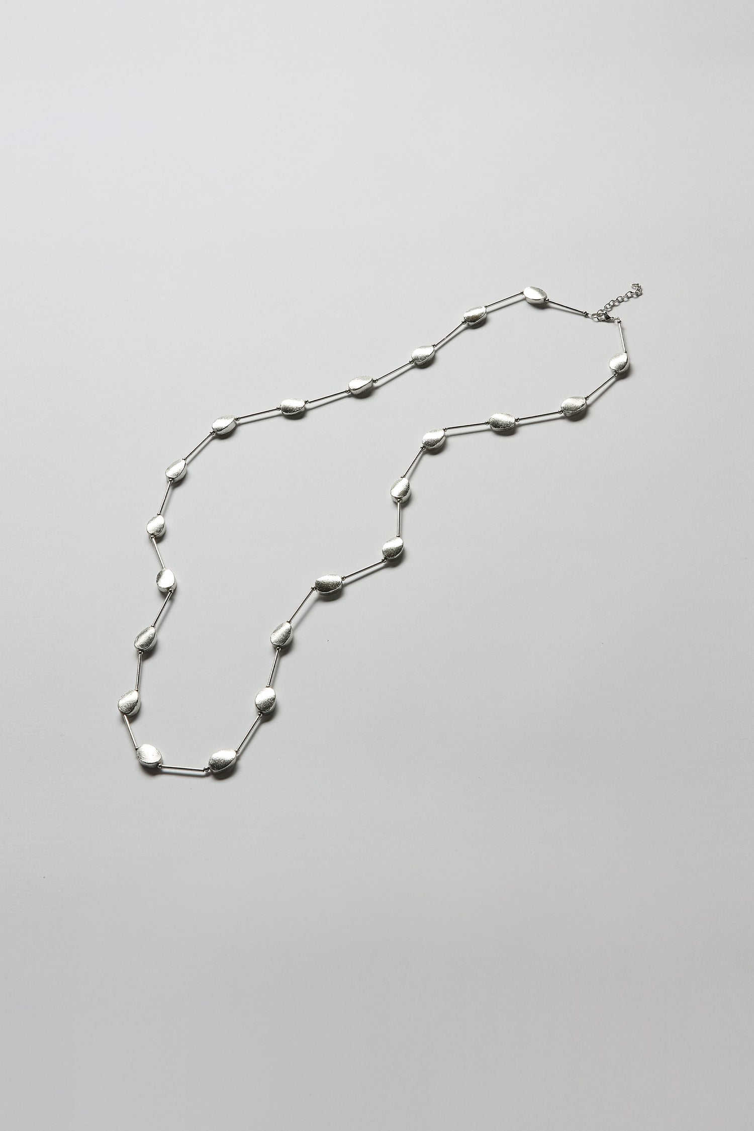 The Oval Silver Disc Necklace features evenly spaced silver oval beads for a look of quiet elegance and modern design, shown against a plain light gray background.