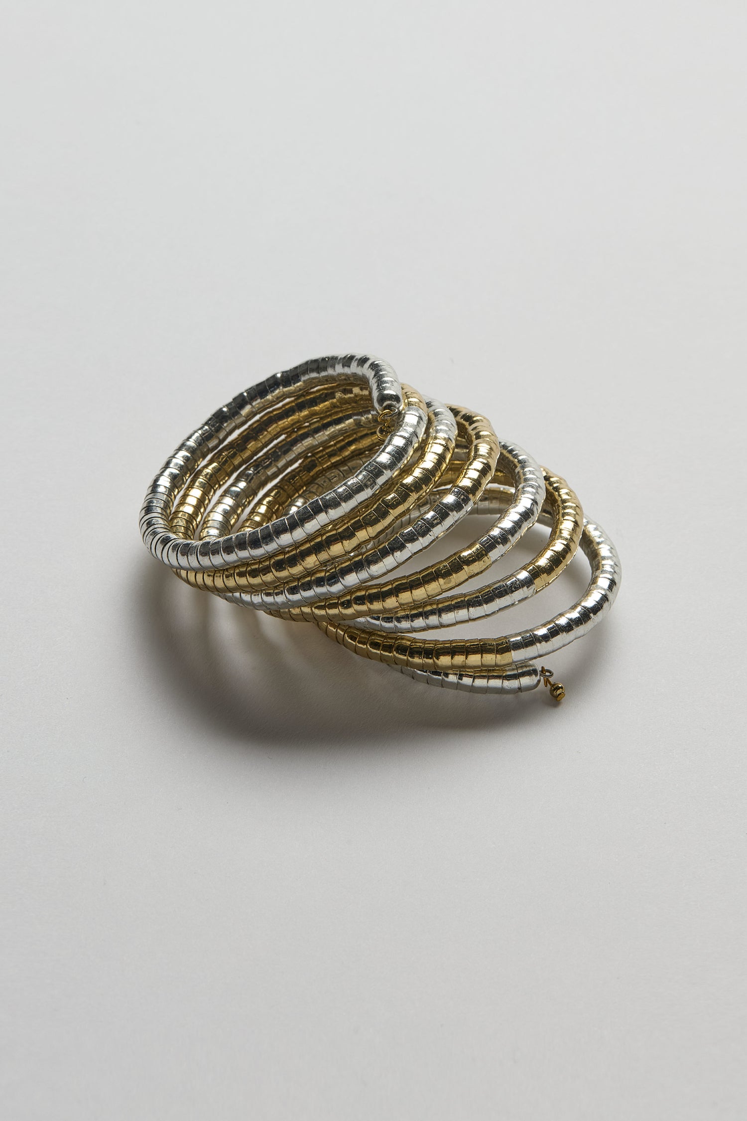 The Mixed Metal Spiral Cuff features a sculptural design with gold and silver tones, showcased in a stacked arrangement on a plain white surface.