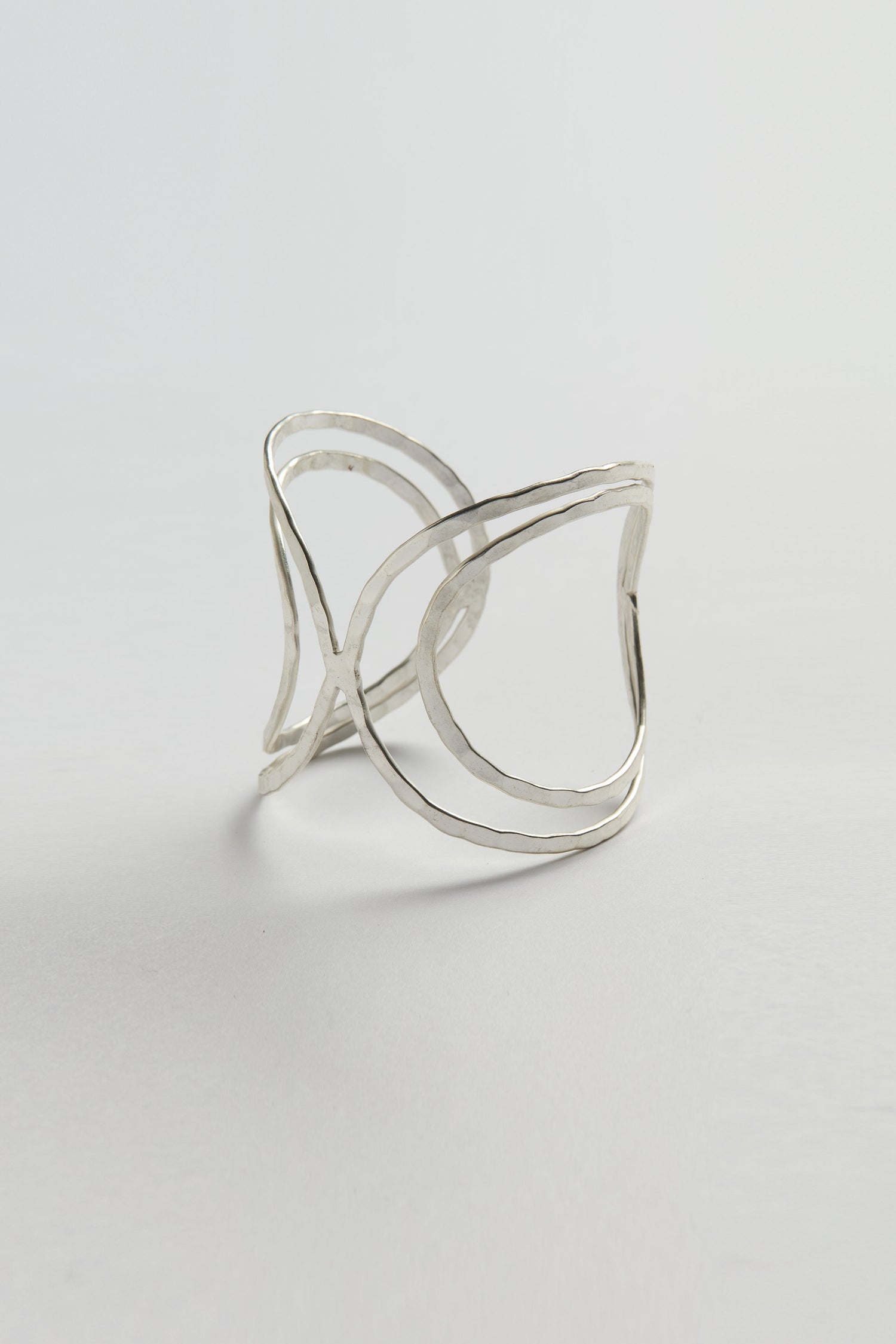 The Butterfly Bangle is a minimalist silver cuff bracelet with an open, abstract leaf-inspired design and sculptural silhouette, showcased against a plain light background.