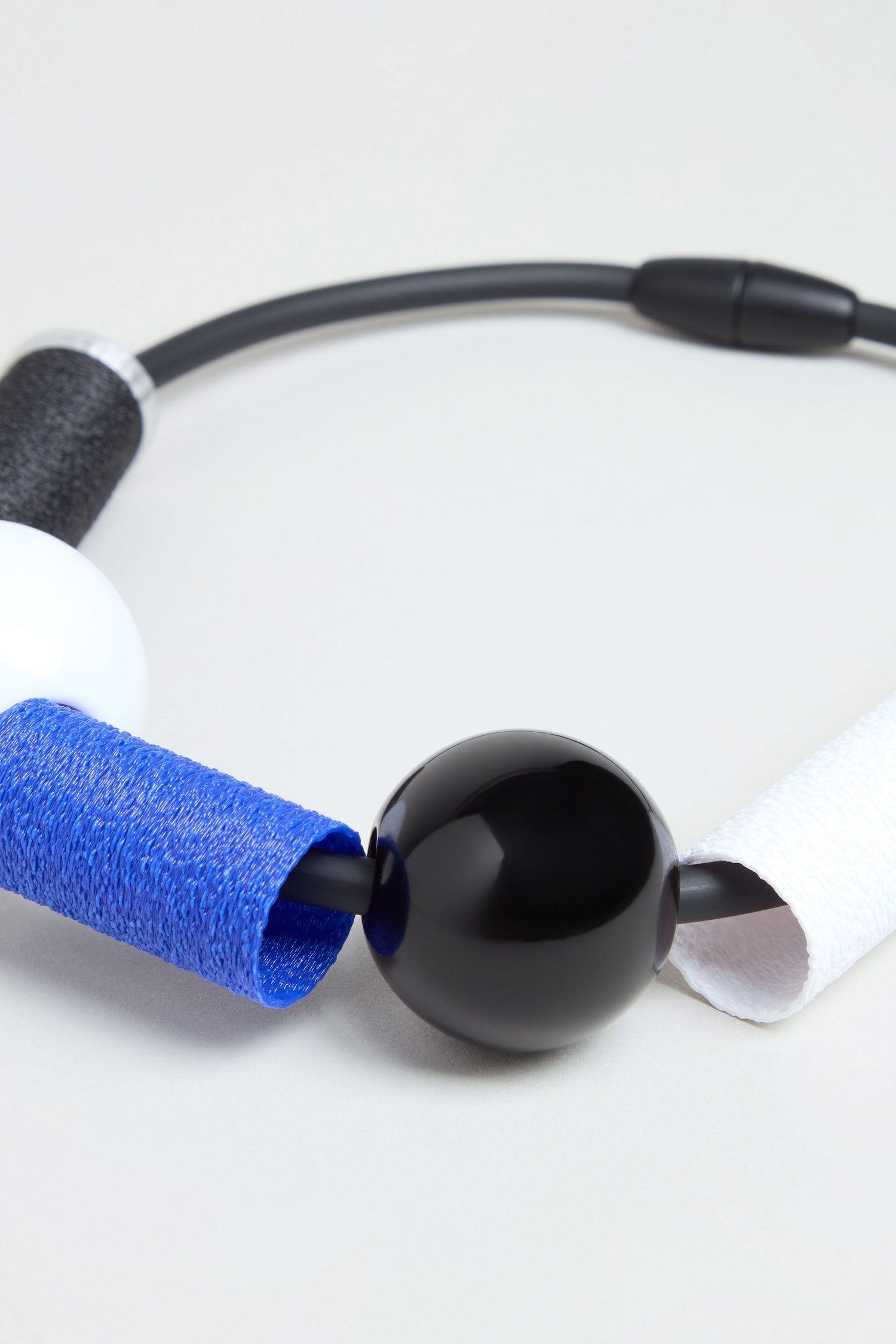 The Colour Block Necklace is a contemporary wearable art piece, featuring large black and white beads, textured blue and white cylindrical segments, and a flexible black cord. Beautifully handmade in France, it is showcased against a neutral background.