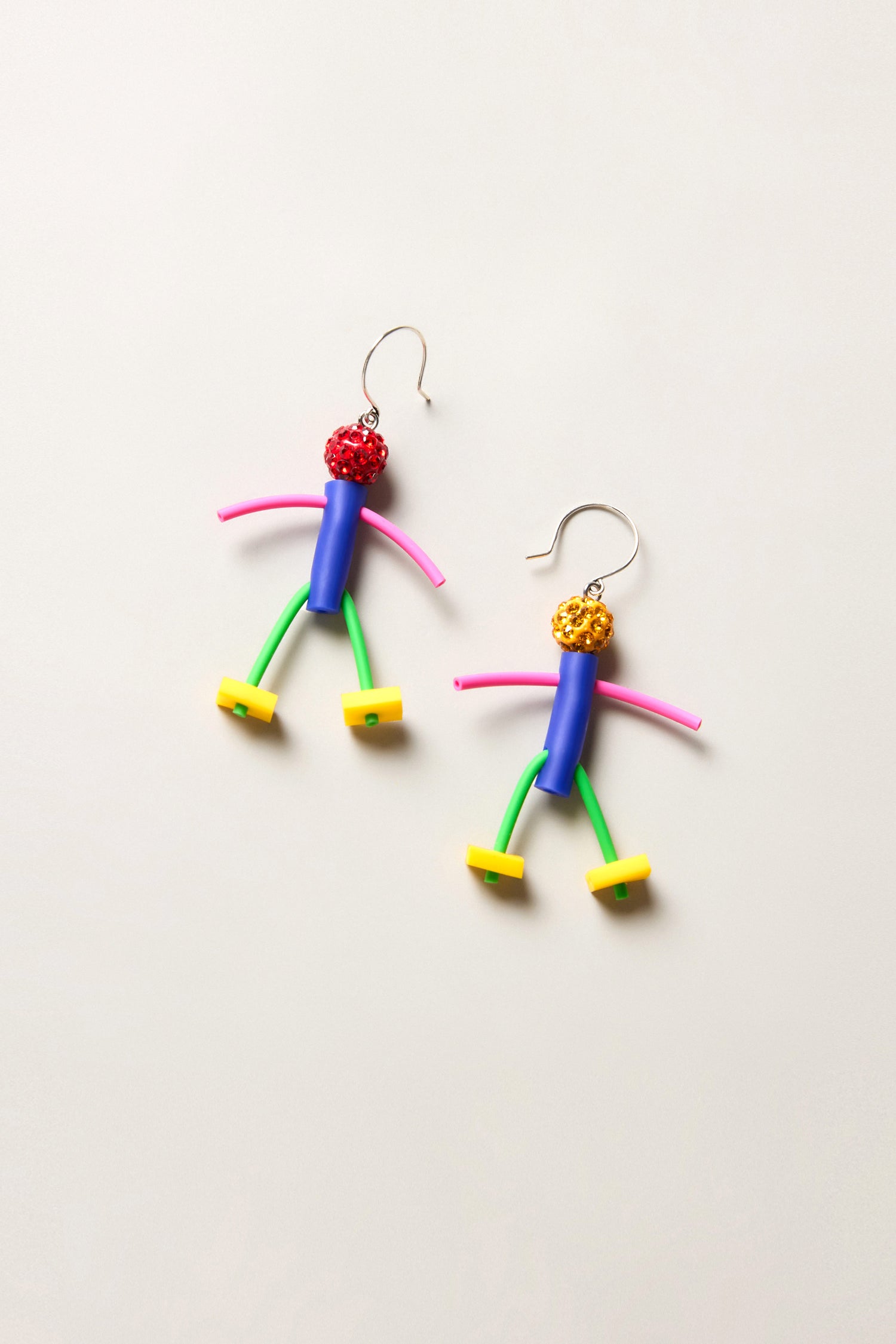 The Beautiful People Earrings are playful, abstract stick figure earrings inspired by Samuel Coraux, crafted from colorful beads and plastic pieces, and shown on a plain light background.