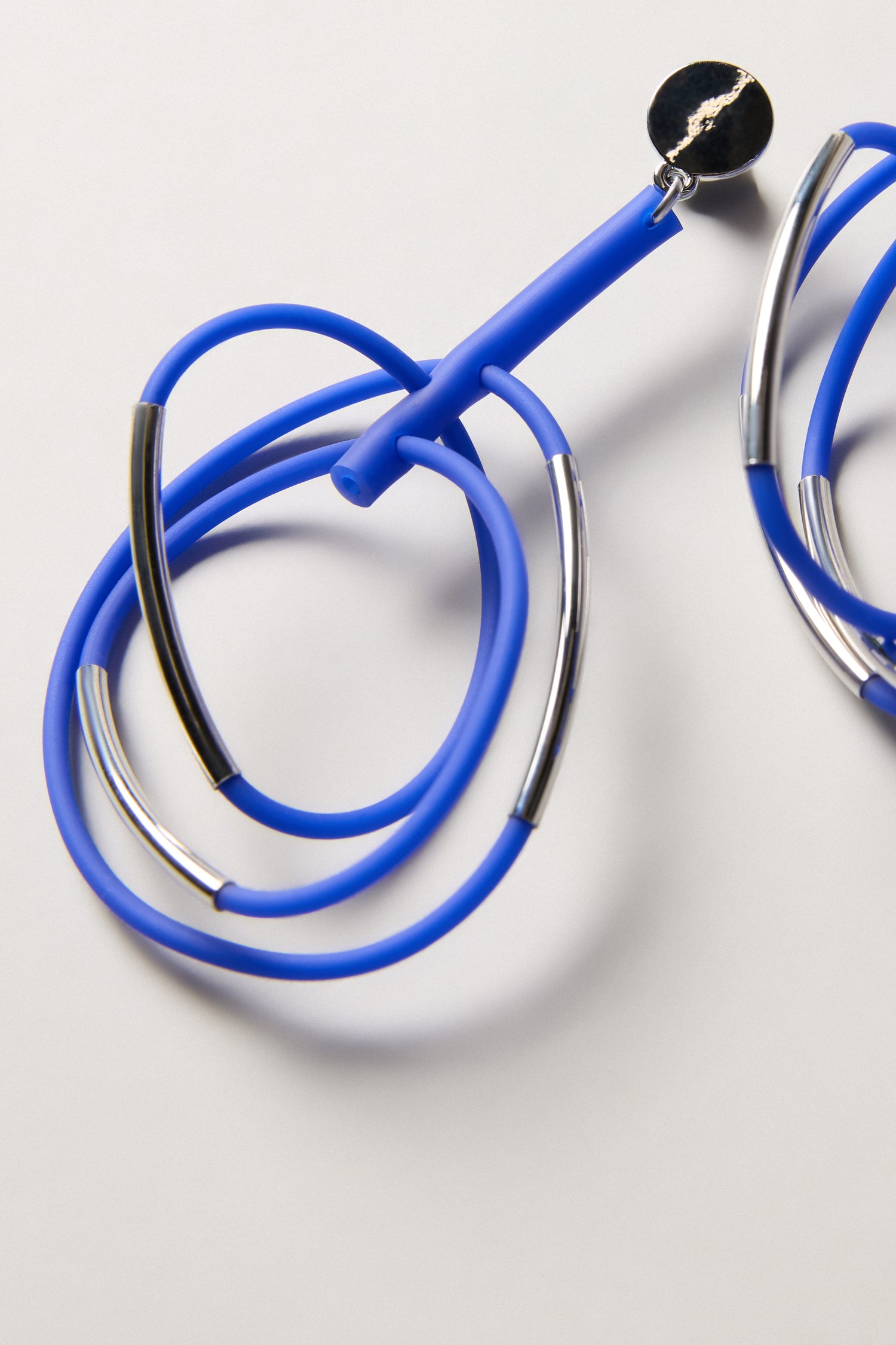 A close-up of Carousel Earrings—blue with silver accents and a black center—coiled on a white surface. Their sleek, modern design brings to mind the elegance of contemporary jewelry.
