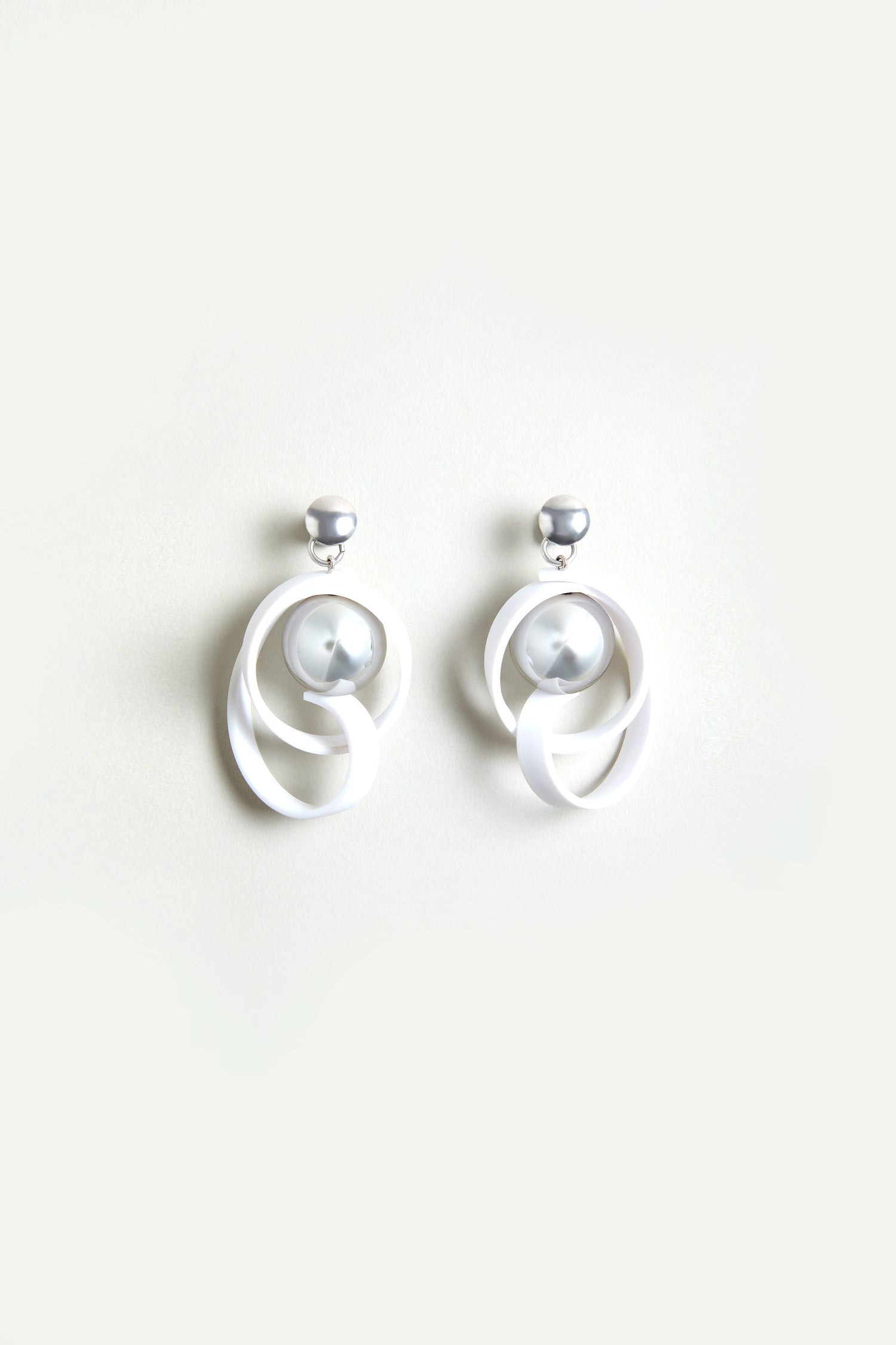 The Silver Sphere Penseur Earrings feature a lightweight design with silver and white loops, a spherical silver stud, and an intertwined circular pattern.