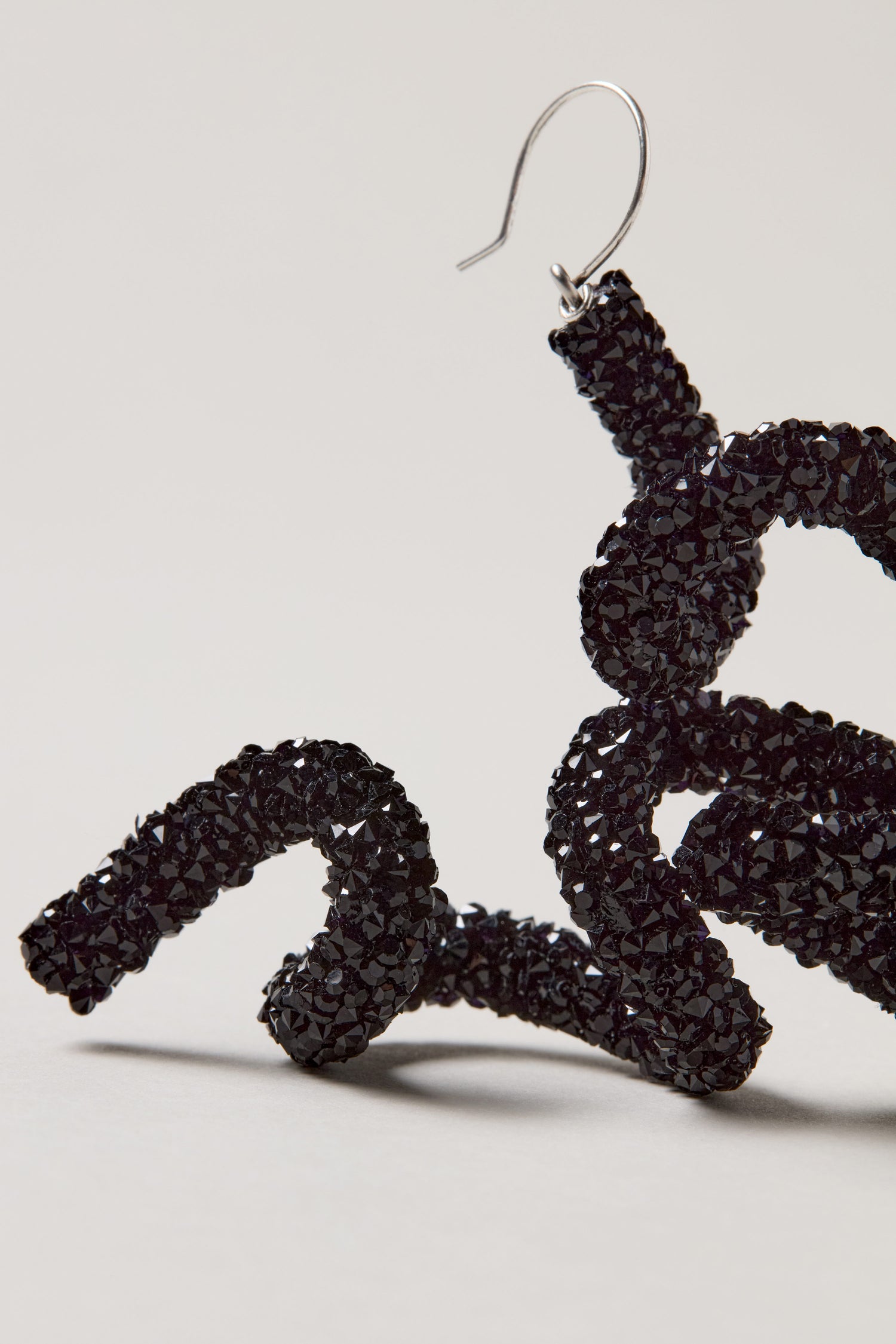 A close-up of the Disco Sketch Black Earrings—a textured, twisted earring with a metal hook—displayed against a plain light background. Ideal for statement jewellery lovers.