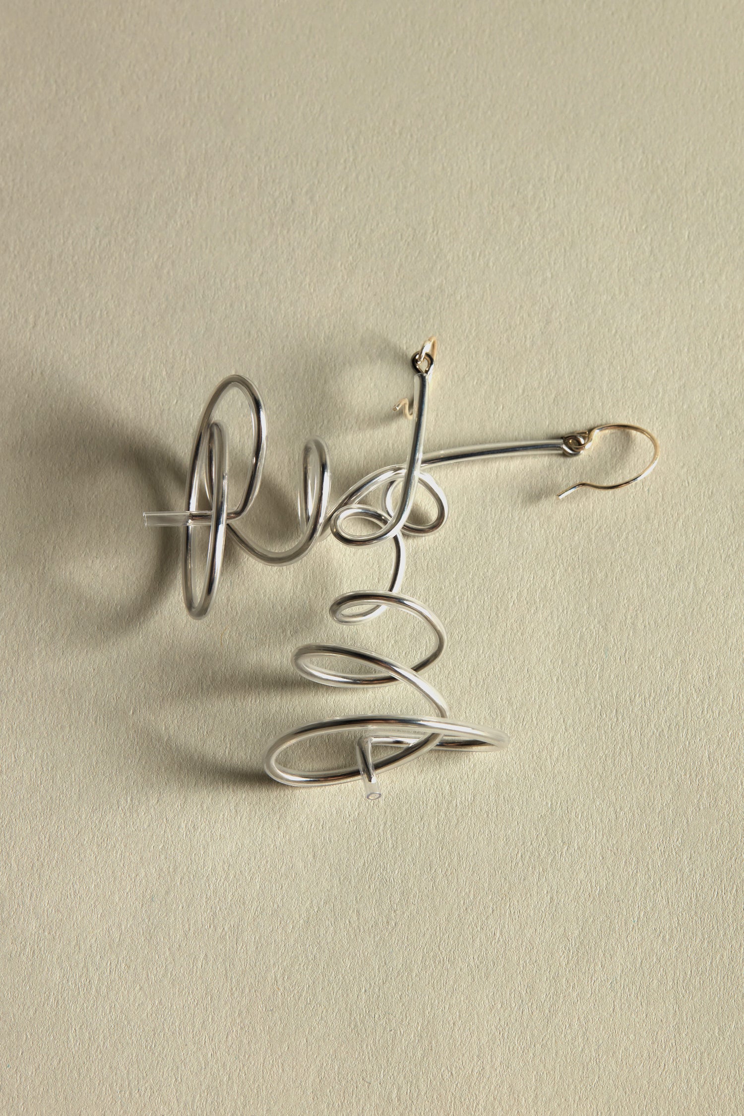 Squiggle Earrings feature delicate silver spirals twisting gracefully, creating a subtle yet striking statement on a plain light background, inspired by Samuel Coraux and making an impact without bold colors.