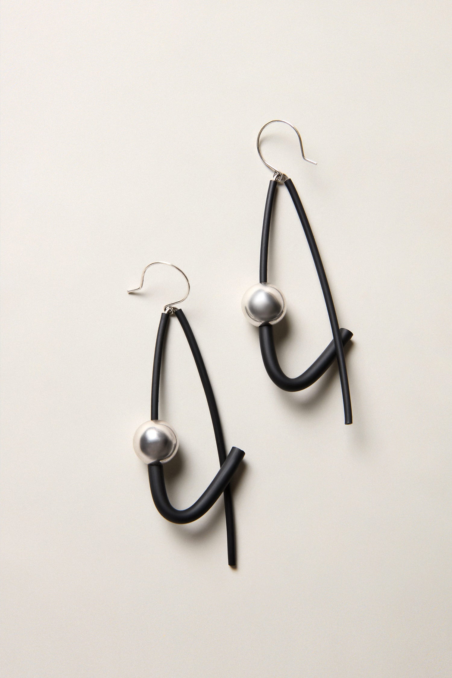 Silver Sphere Earrings: Abstract black drop earrings featuring curved lines and silver sphere accents, displayed on a light neutral background—an eye-catching example of modern jewellery design.