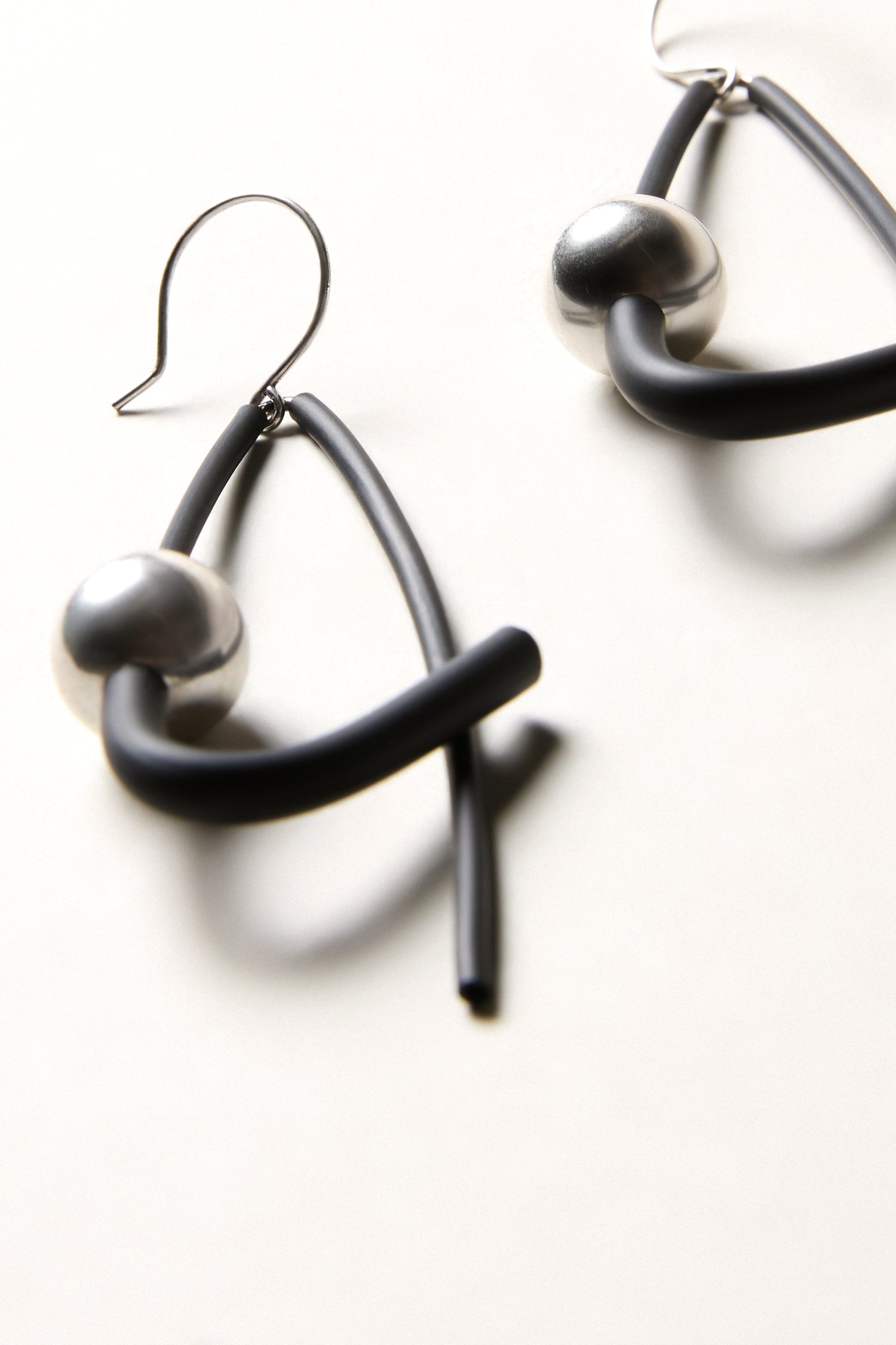 The Silver Sphere Earrings feature abstract silver spheres with black curved rods and round silver beads, reflecting Samuel Coraux’s sculptural jewellery style, and are showcased on a neutral background.