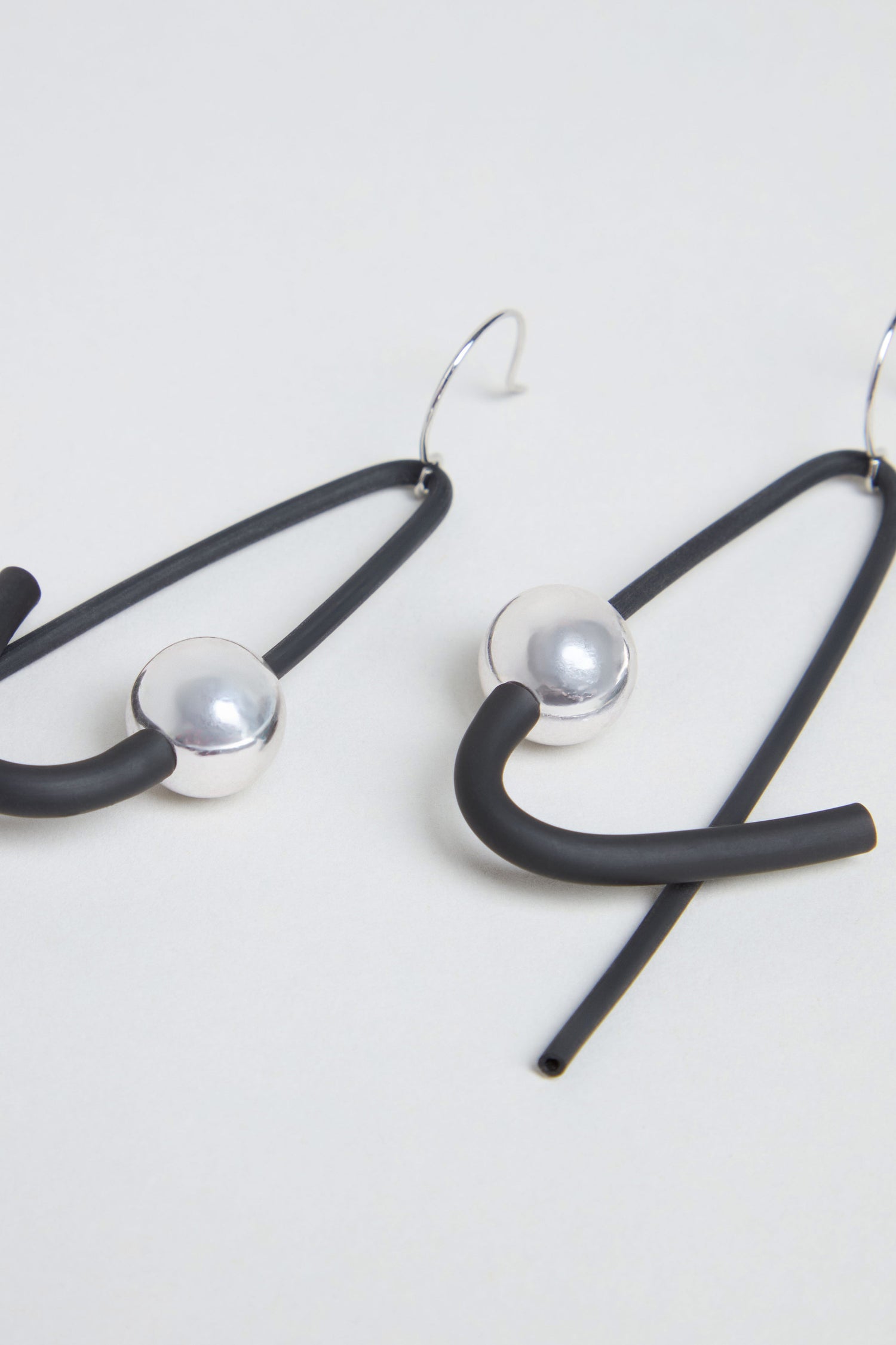 The Sphere Earrings are a pair of contemporary, handmade earrings from Paris featuring black rubber loops, silver-tone spherical beads, and metal hooks, elegantly displayed on a light background.
