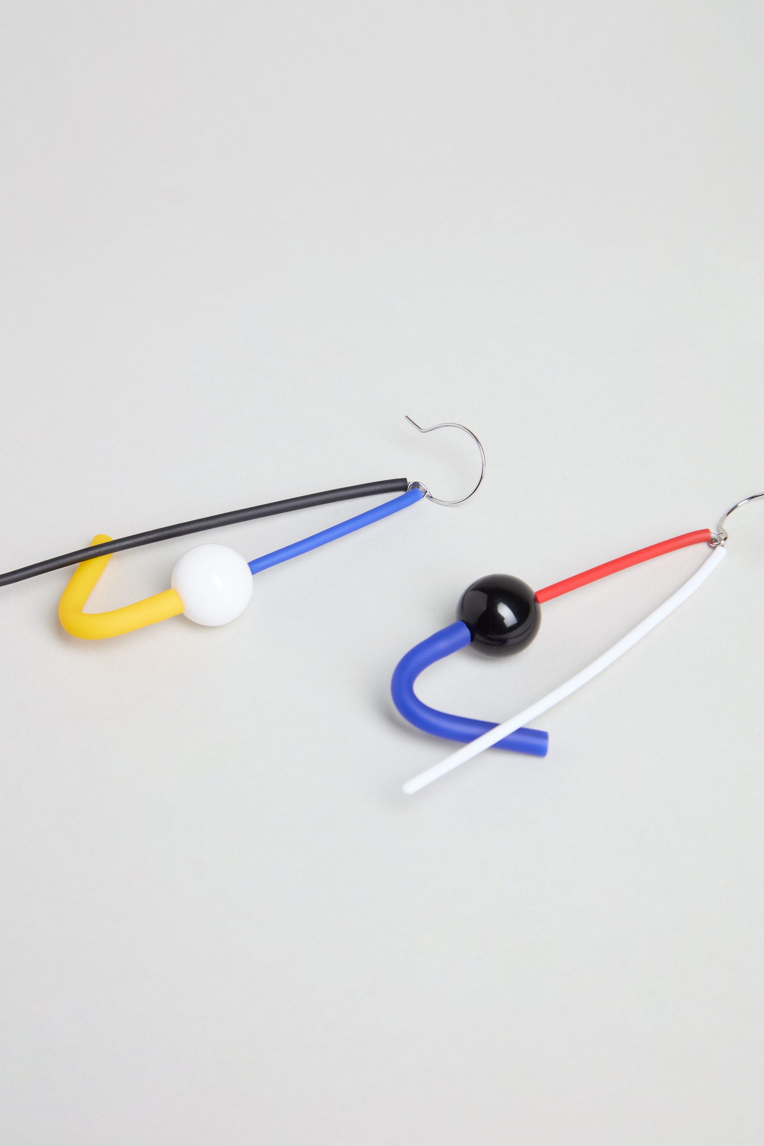 The Kandinsky Sphere Earrings are handmade in Paris and feature asymmetrical geometric designs in primary colors—one earring with yellow, black, blue, and white; the other with red, blue, black, and white.