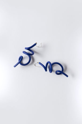 The Sketch Earrings by Samuel Coraux are blue sculptural spiral earrings crafted from lightweight rubber with silver hooks, shown on a plain white background.
