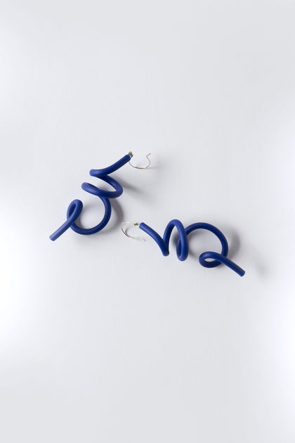 The Sketch Earrings by Samuel Coraux are blue sculptural spiral earrings crafted from lightweight rubber with silver hooks, shown on a plain white background.