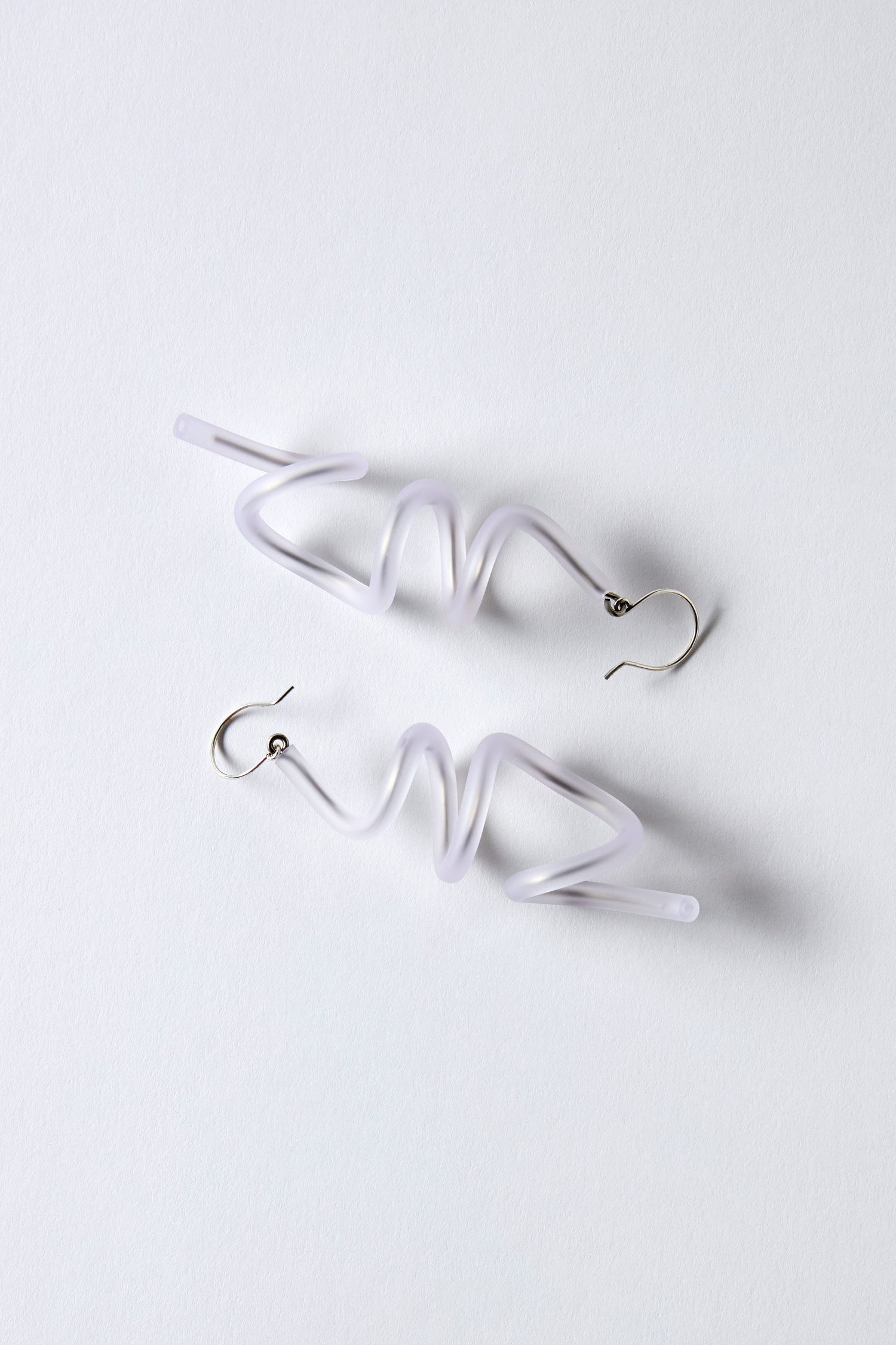The Sketch Earrings feature silver hooks and irregular, zigzag-shaped translucent white rubber bodies reminiscent of Samuel Coraux's sculptural spiral style, displayed on a white background. Lightweight and bold, they highlight creative design.