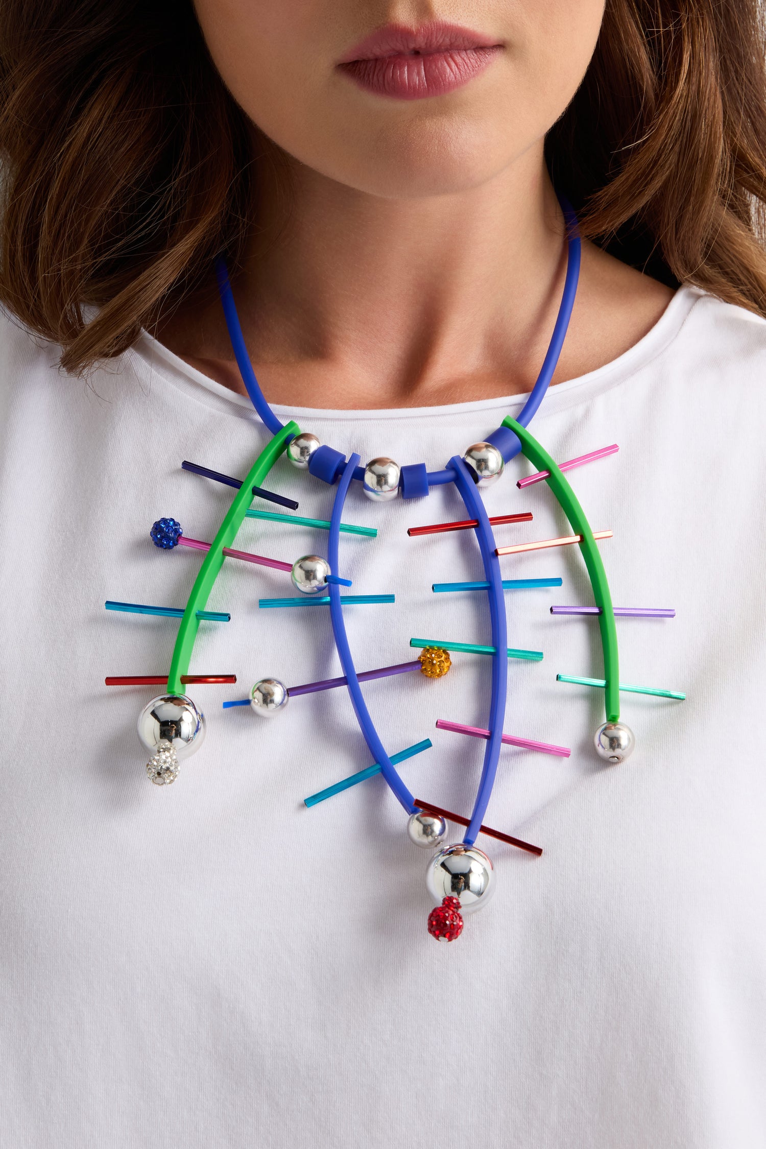 A woman wears a white shirt and the Fame Necklace by Samuel Coraux—handmade in Paris with blue and green tubes, silver spheres, and multicolored sticks.