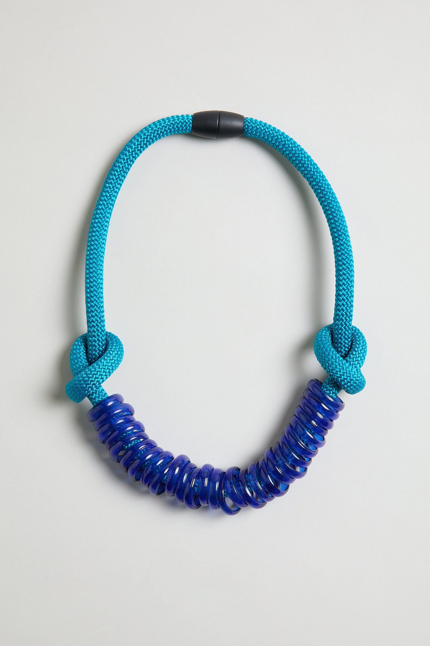 The Murano Glass Rings Necklace features a thick blue textured rope cord with two knots on each side and several translucent Murano glass rings strung at the center.