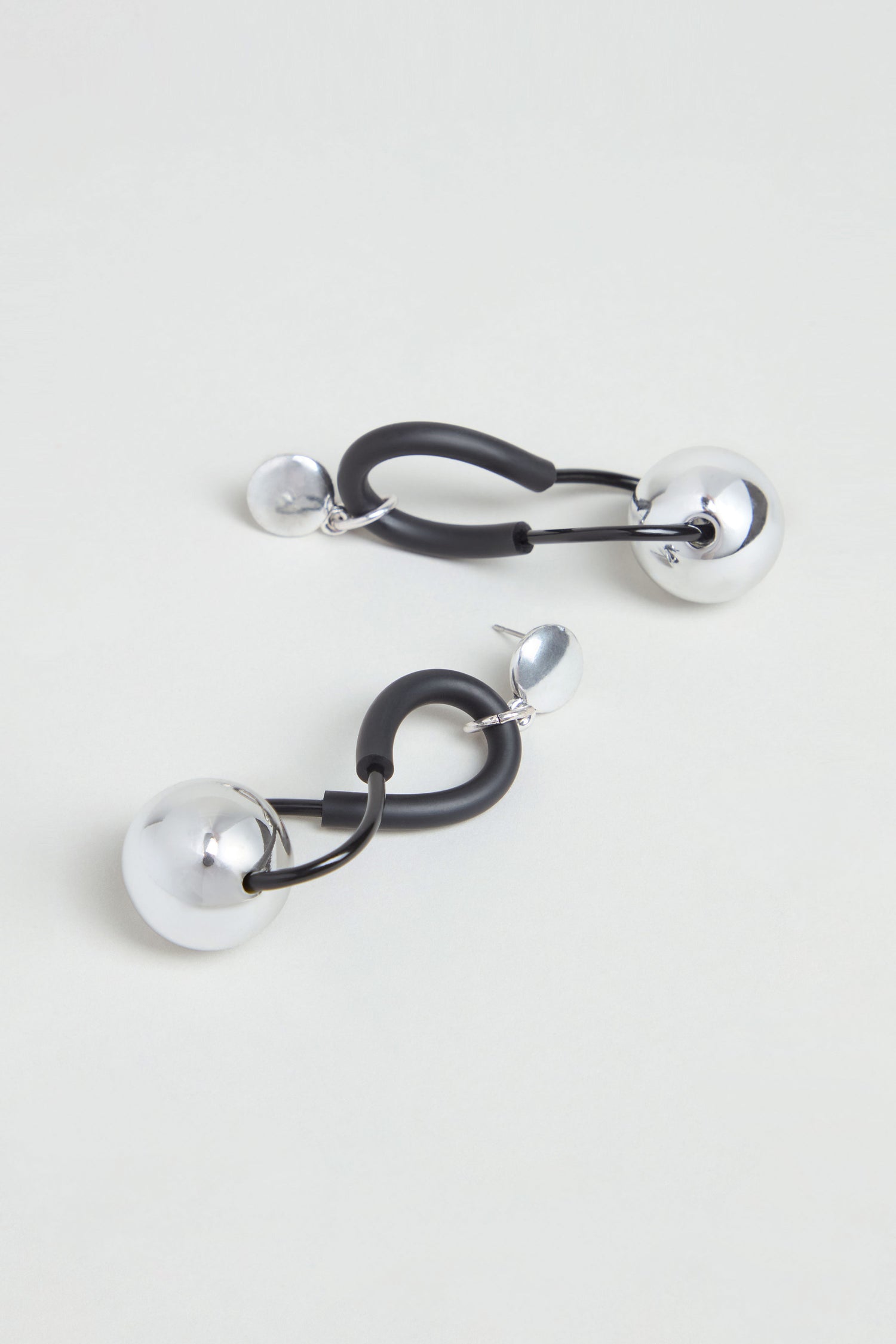 Infinity Earrings – A pair of modern drop earrings featuring large and small silver spheres connected by black curved elements, showcased against a light background. The sculptural design of the handmade Infinity Earrings reflects French artistry, blending unique elegance with contemporary style.