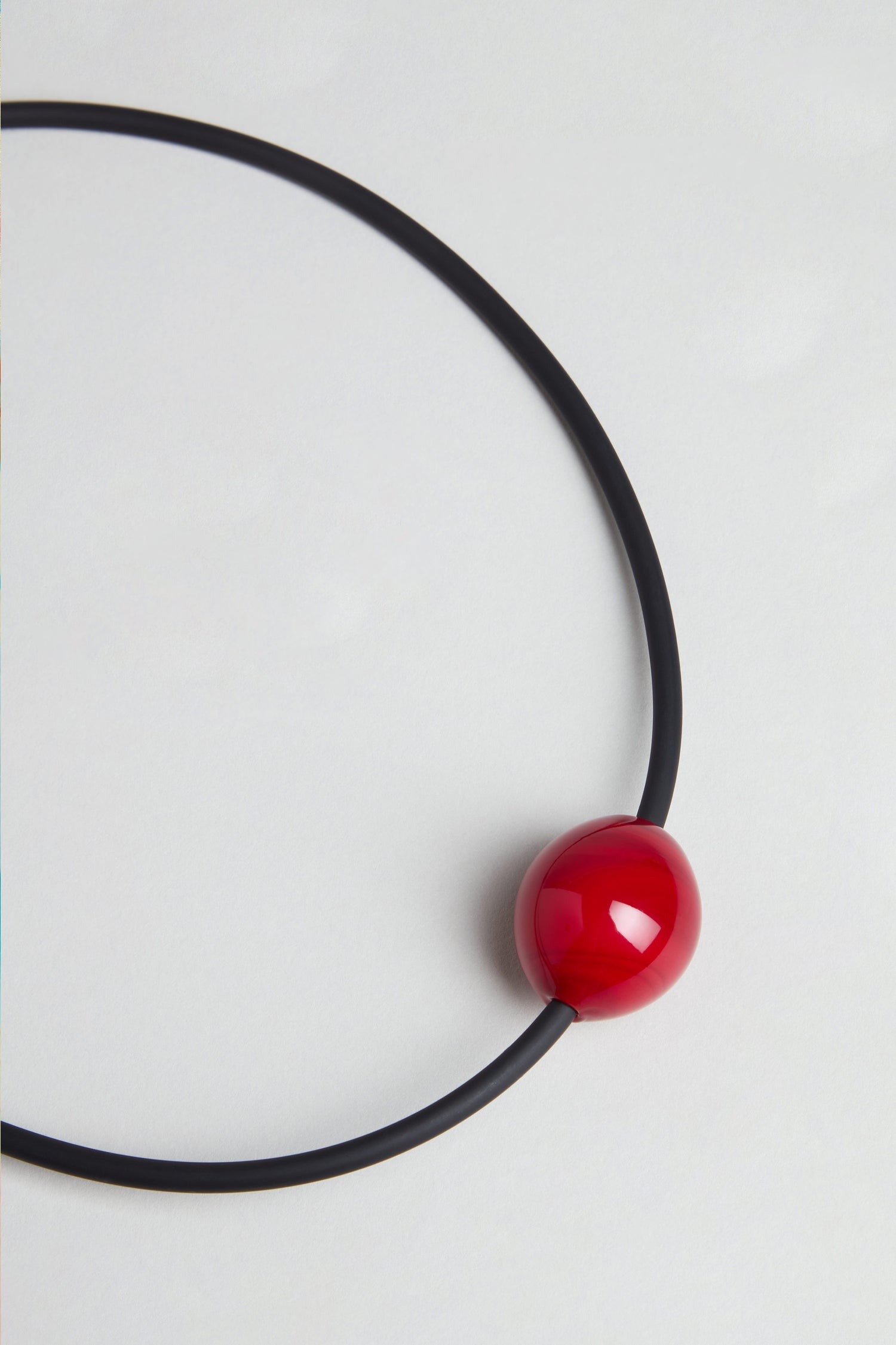 The Murano Bead Necklace is a handmade minimalist piece from Paris with a black circular design and a glossy red Murano bead near the bottom, shown on a plain white background.