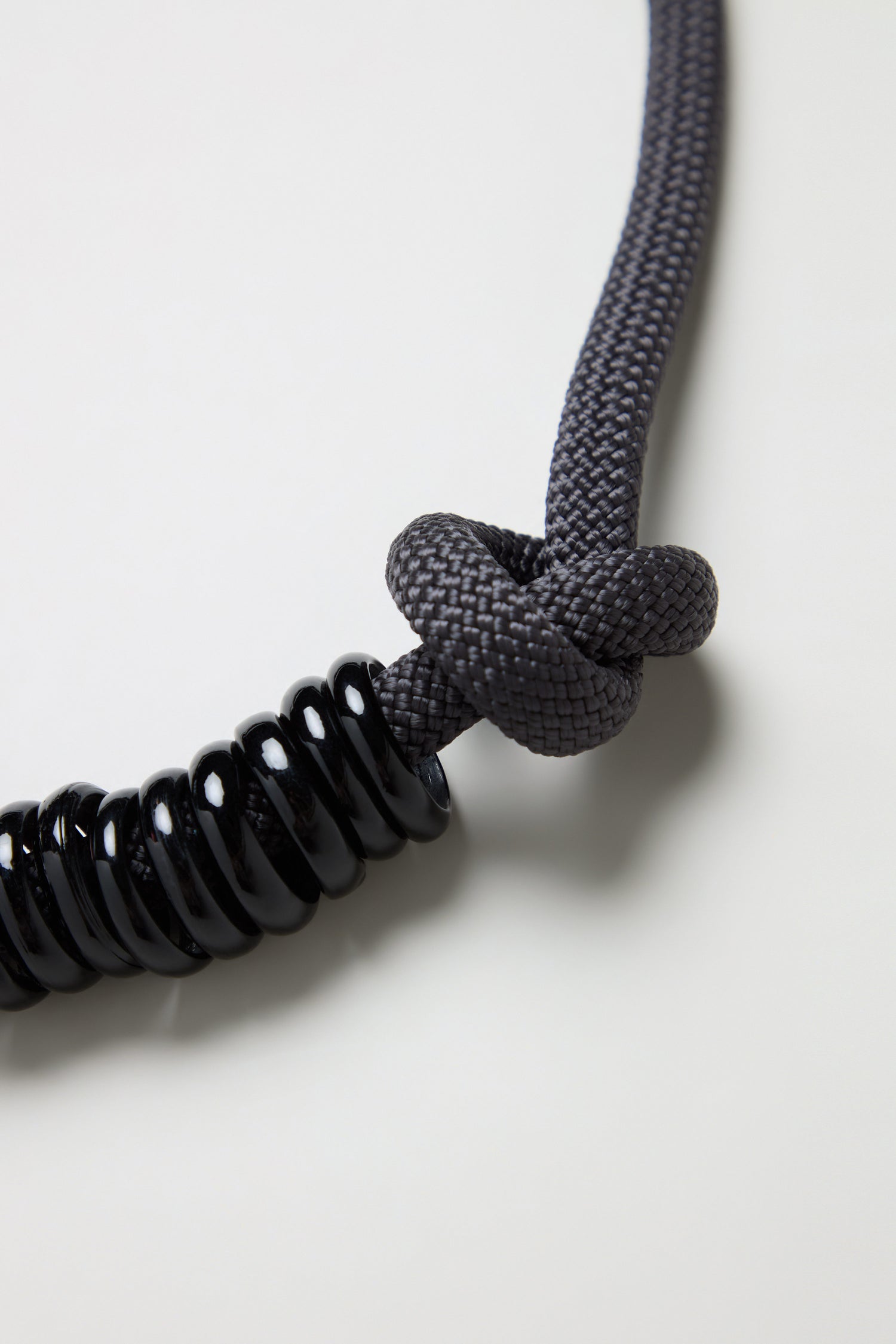 Close-up of the Murano Glass Rings Necklace: a gray braided rope knotted with chunky glass rings looped at one end, creating a unique statement piece against a plain light background.