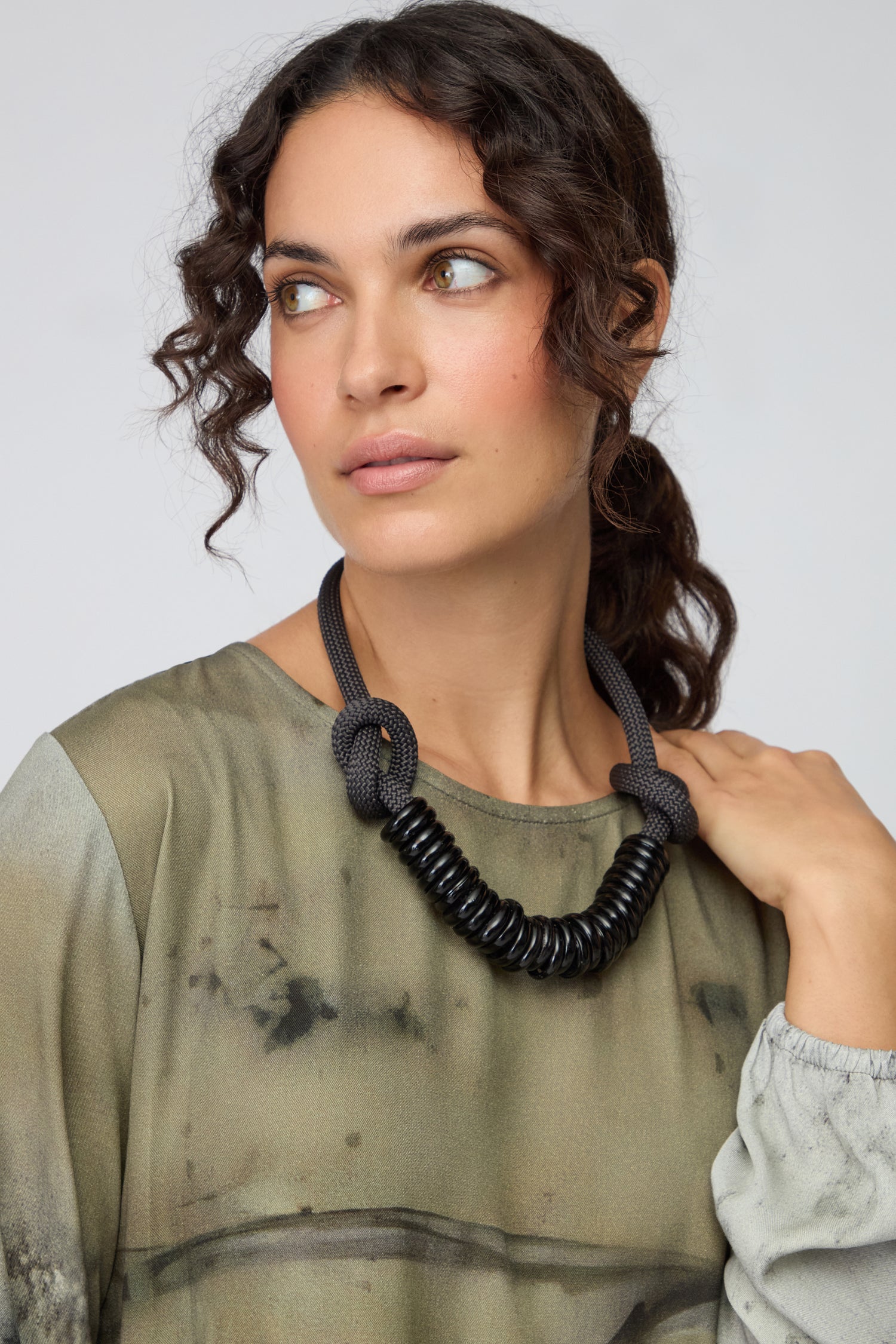 Woman with curly hair wearing a green top and the Murano Glass Rings Necklace, looking slightly to the side against a plain background—her necklace showcasing wearable art at its finest.