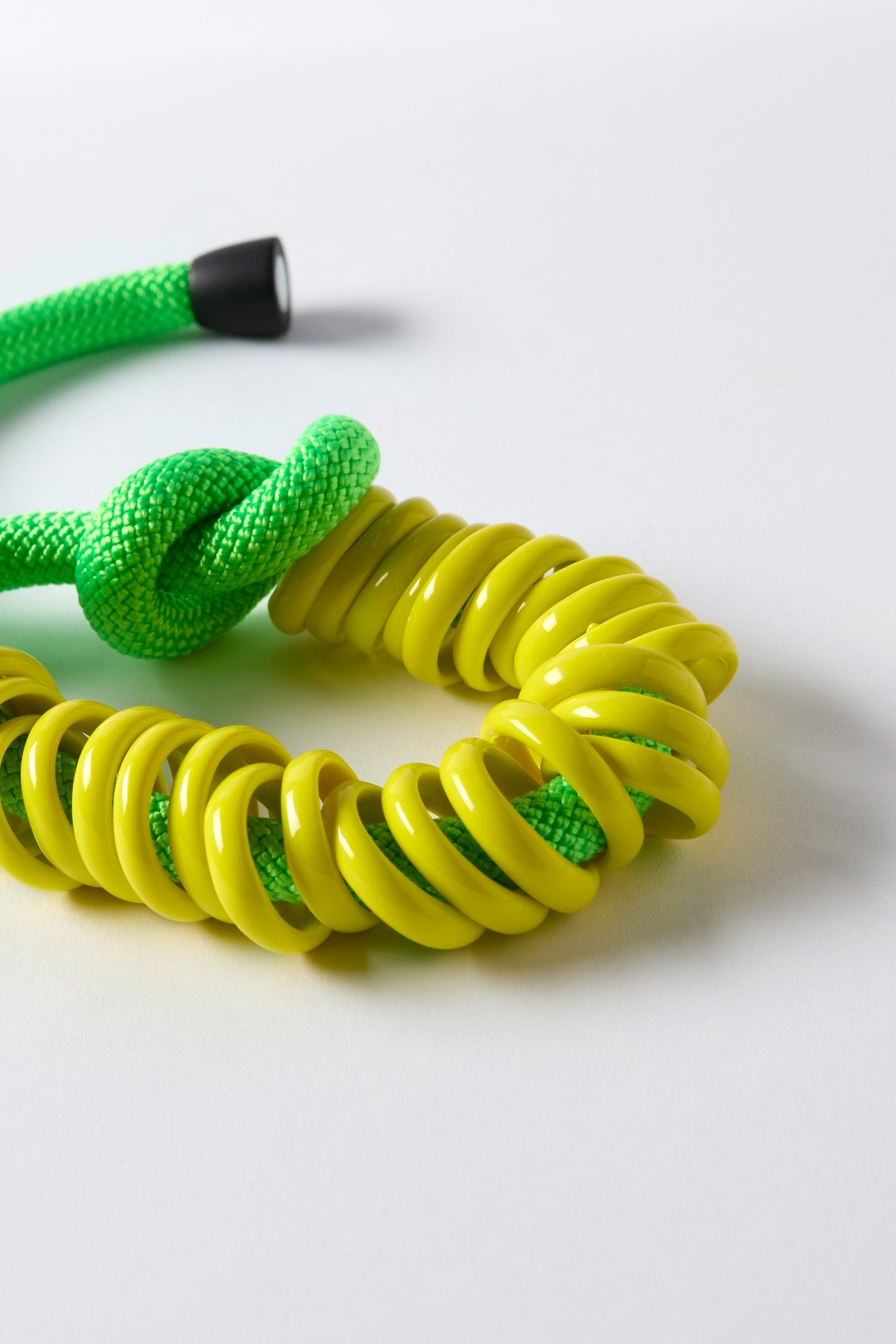 The Murano Glass Rings Necklace features a green rope with a knot, threaded through glossy yellow chunky glass rings, arranged on a white surface—ideal as sculptural jewelry or a bold statement necklace.