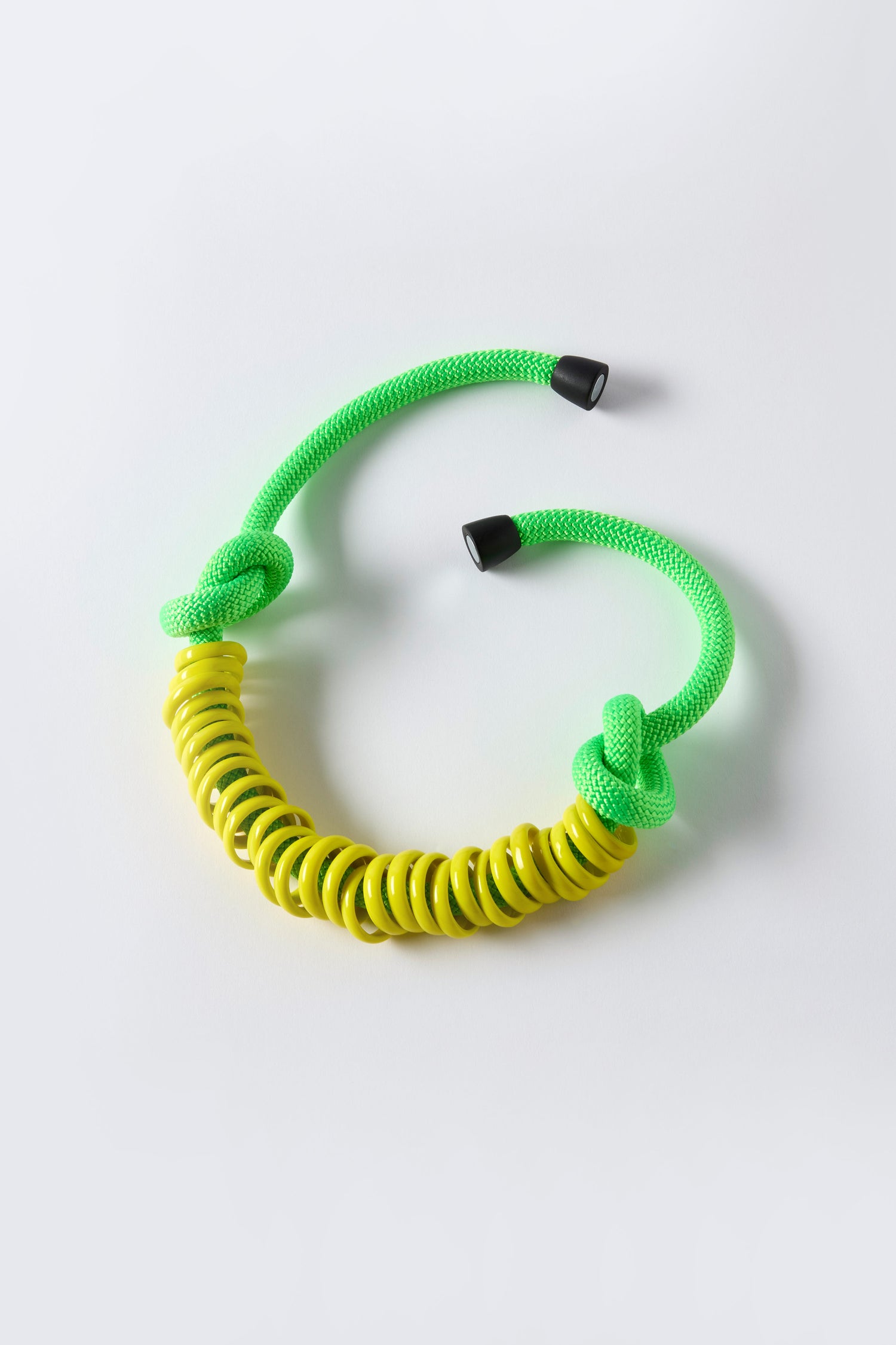 The Murano Glass Rings Necklace features a vibrant green braided cord, black end caps, and central yellow spiral beads—a striking choice for fans of sculptural jewelry.