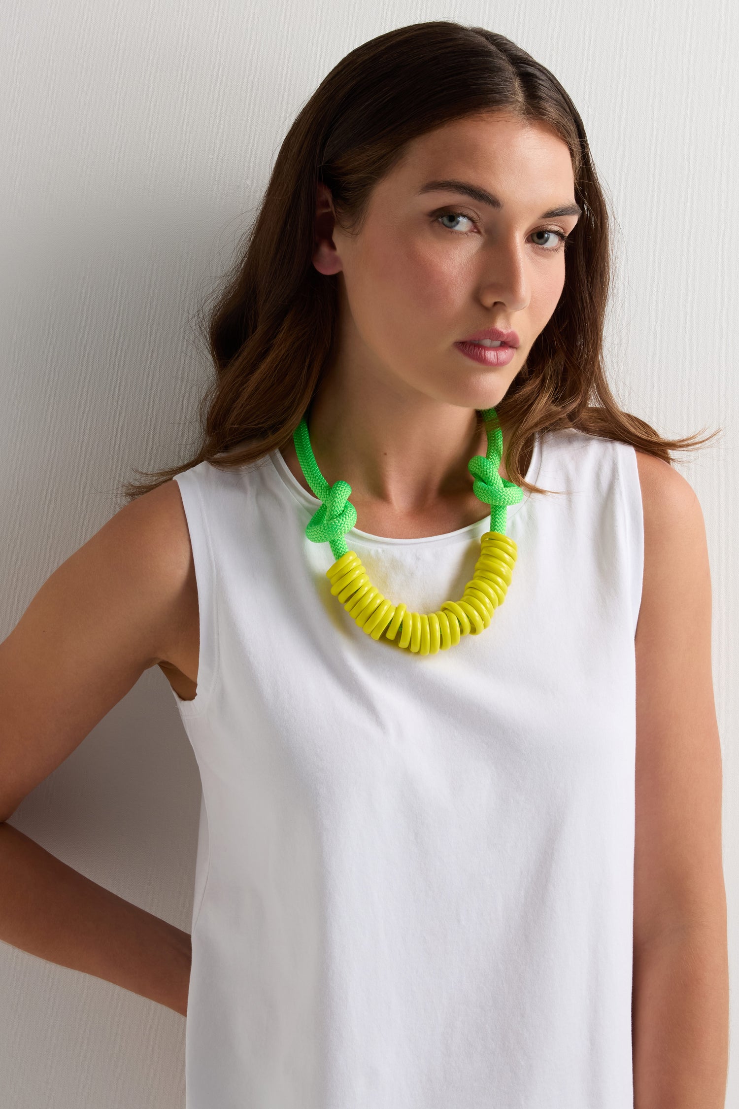A woman wears the Murano Glass Rings Necklace, a sculptural statement piece with chunky green and yellow rings, paired with a sleeveless white top against a plain white background.