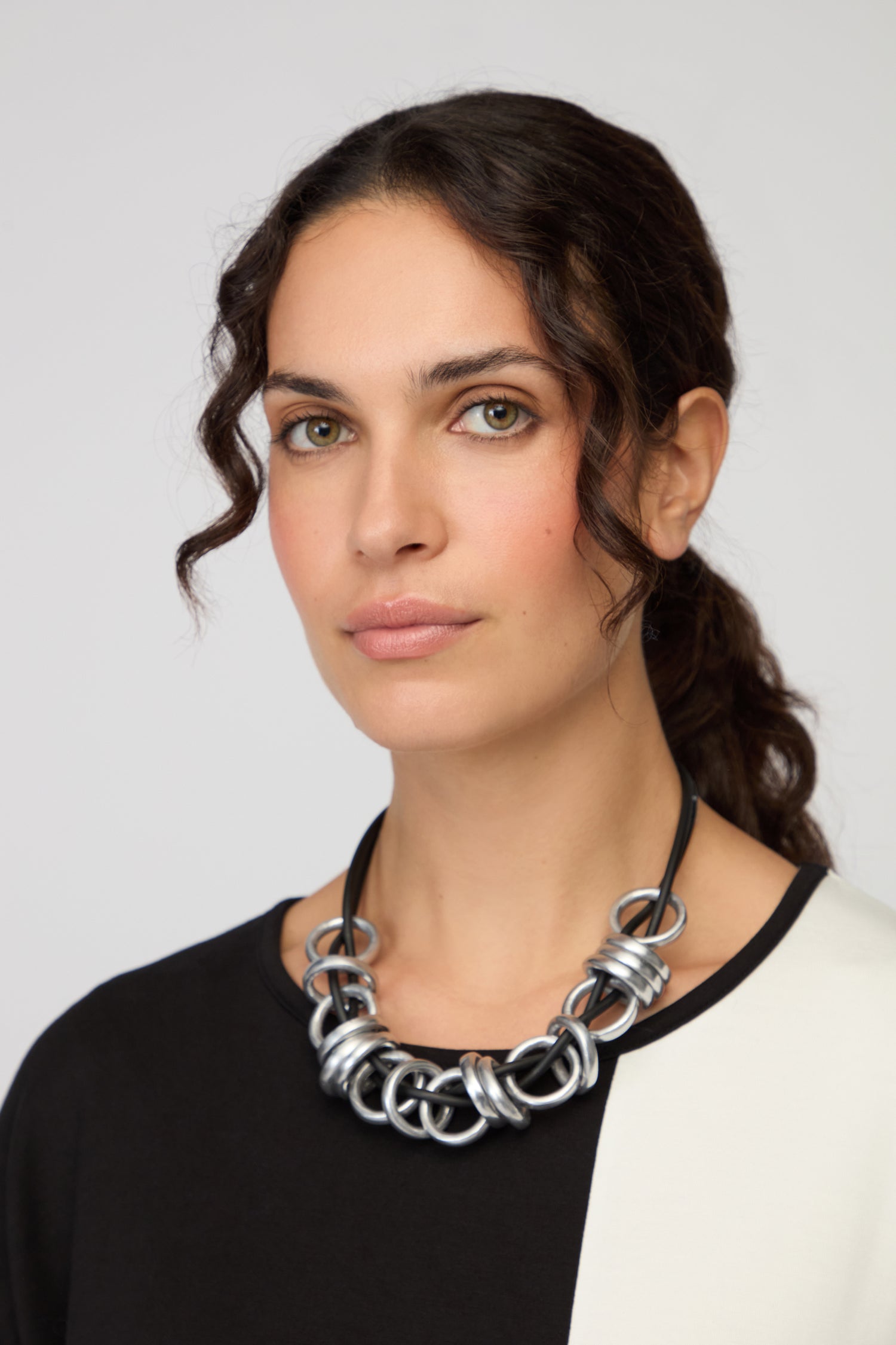 A woman with wavy dark hair in a ponytail wears a black and white top and a bold Black and Silver Metal Rings Necklace, facing the camera against a plain background.