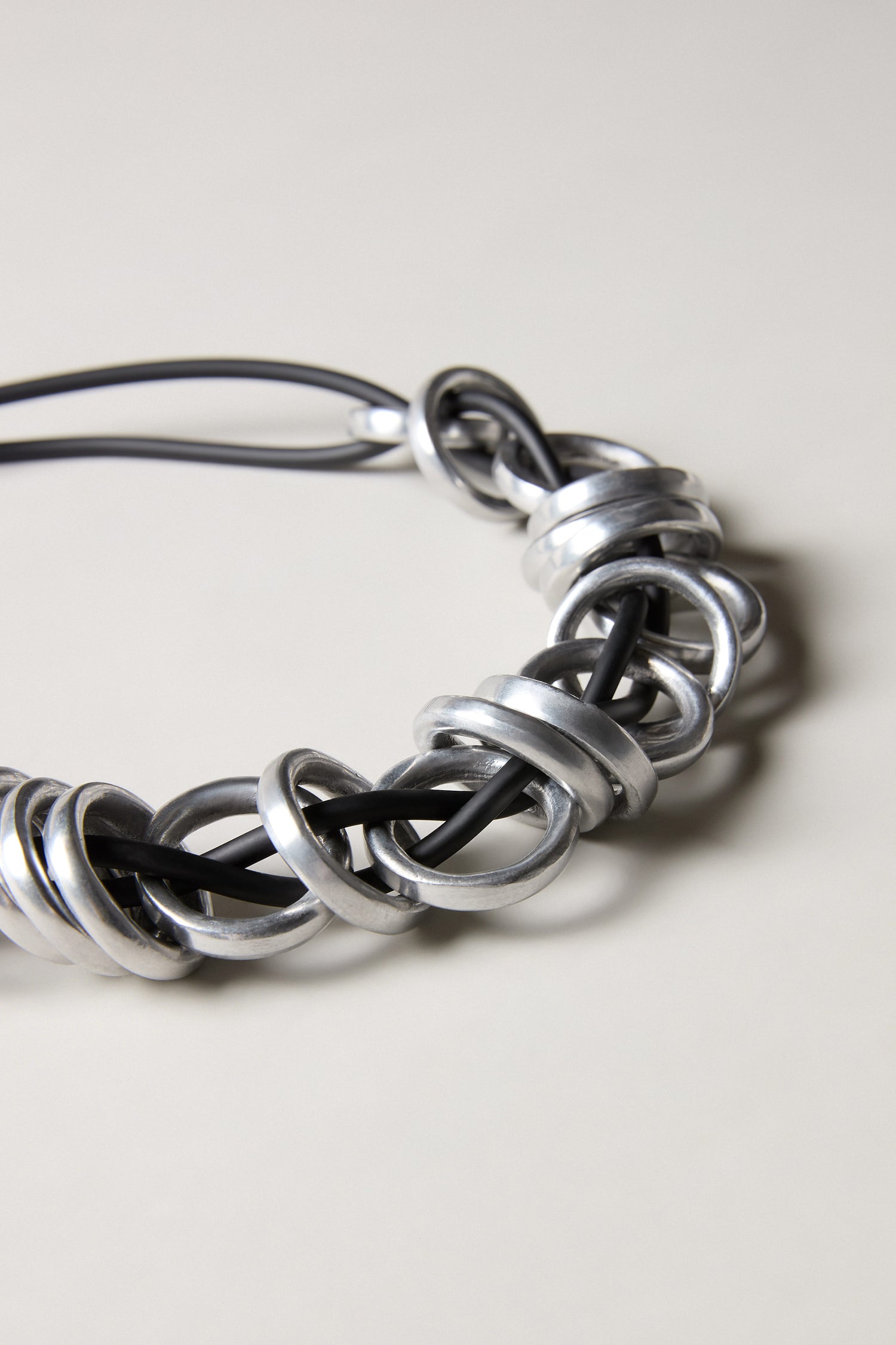 The Black and Silver Metal Rings Necklace features interlocking silver rings on a black cord, creating a bold contemporary look, and is showcased against a neutral background.