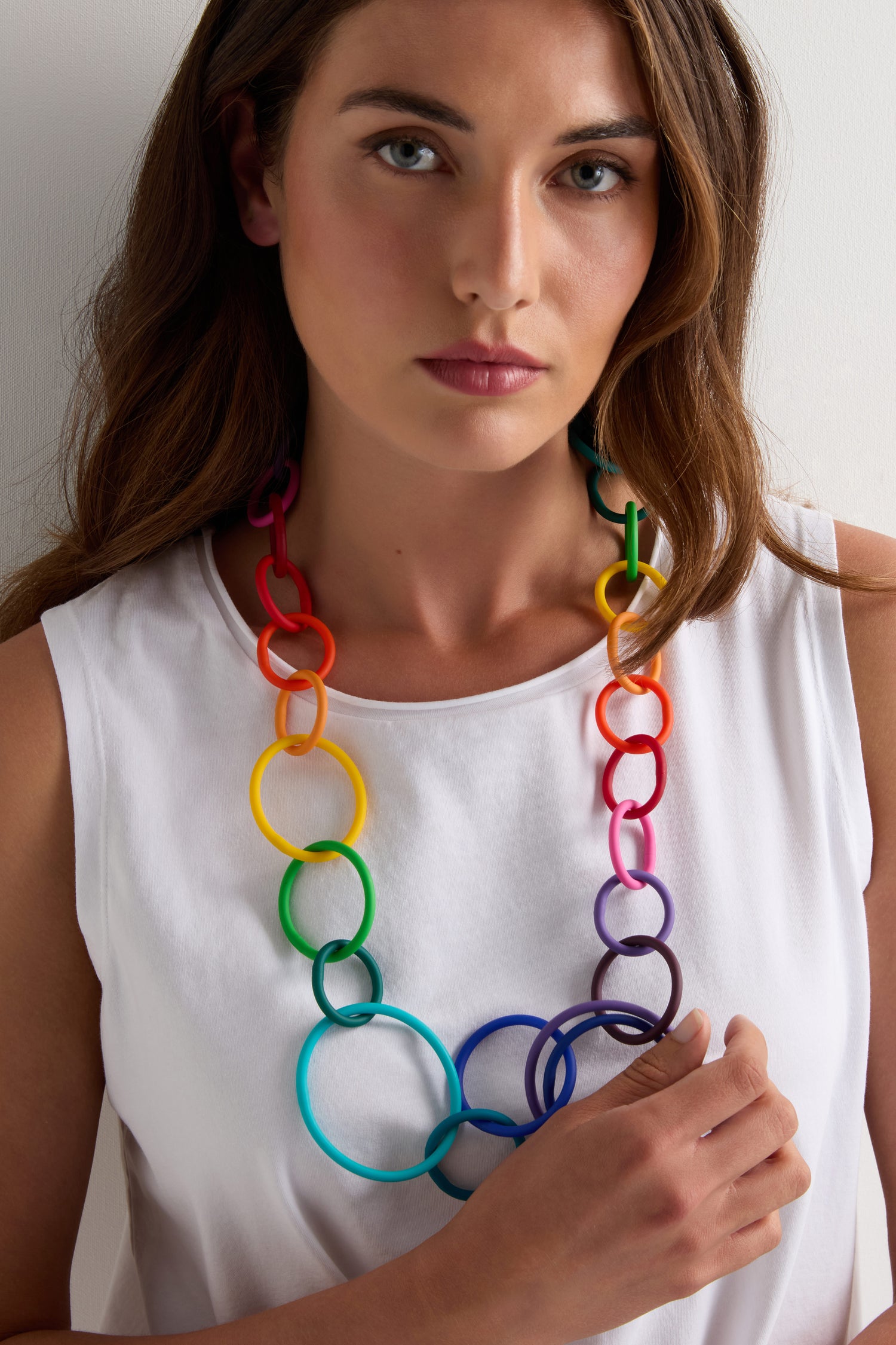 A woman wearing a white sleeveless top and the Long Rainbow Hoops Necklace by Samuel Coraux, looking directly at the camera.