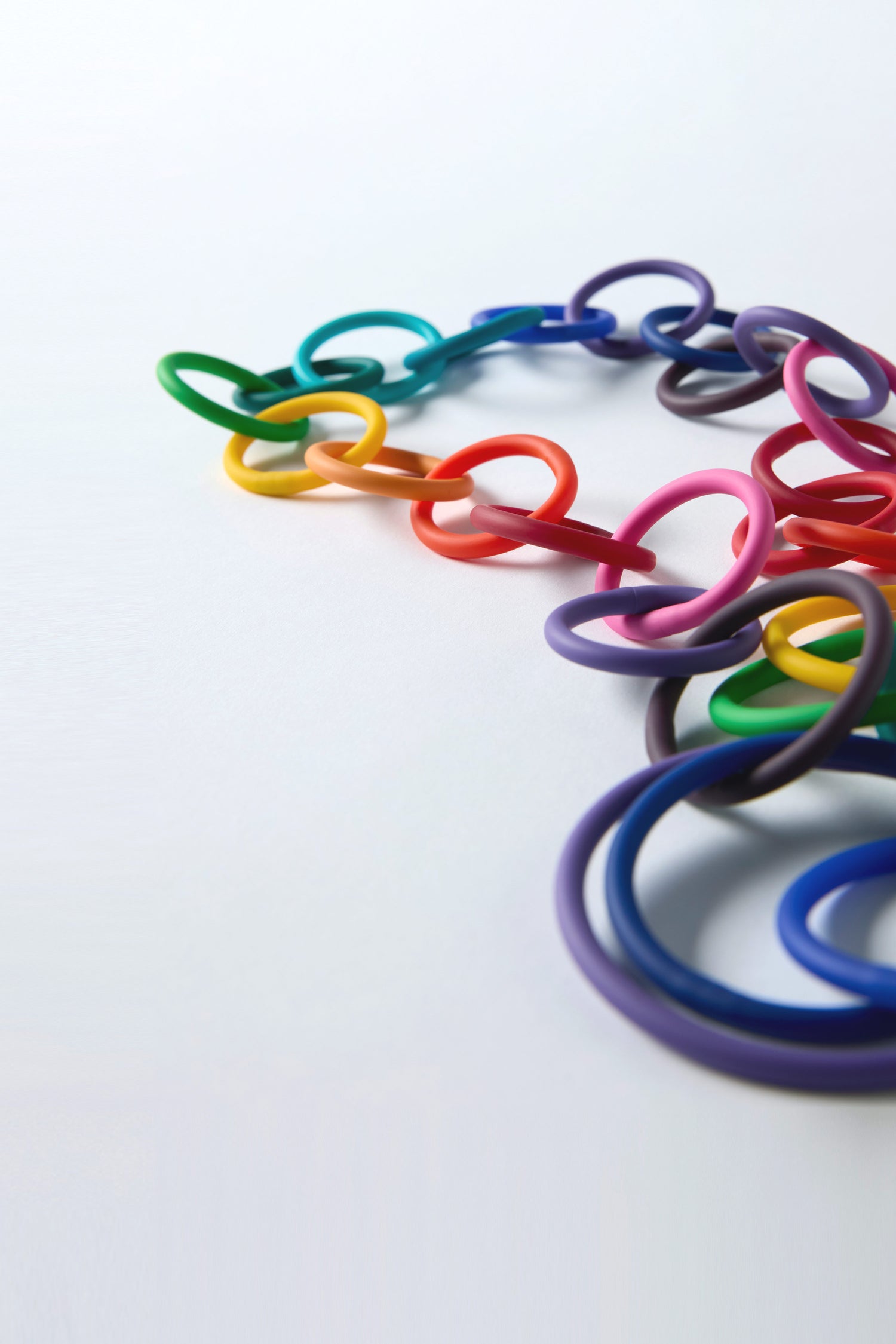 A close-up of interlinked, colorful plastic rings arranged in a chain on a white surface, showcasing the Long Rainbow Hoops Necklace.